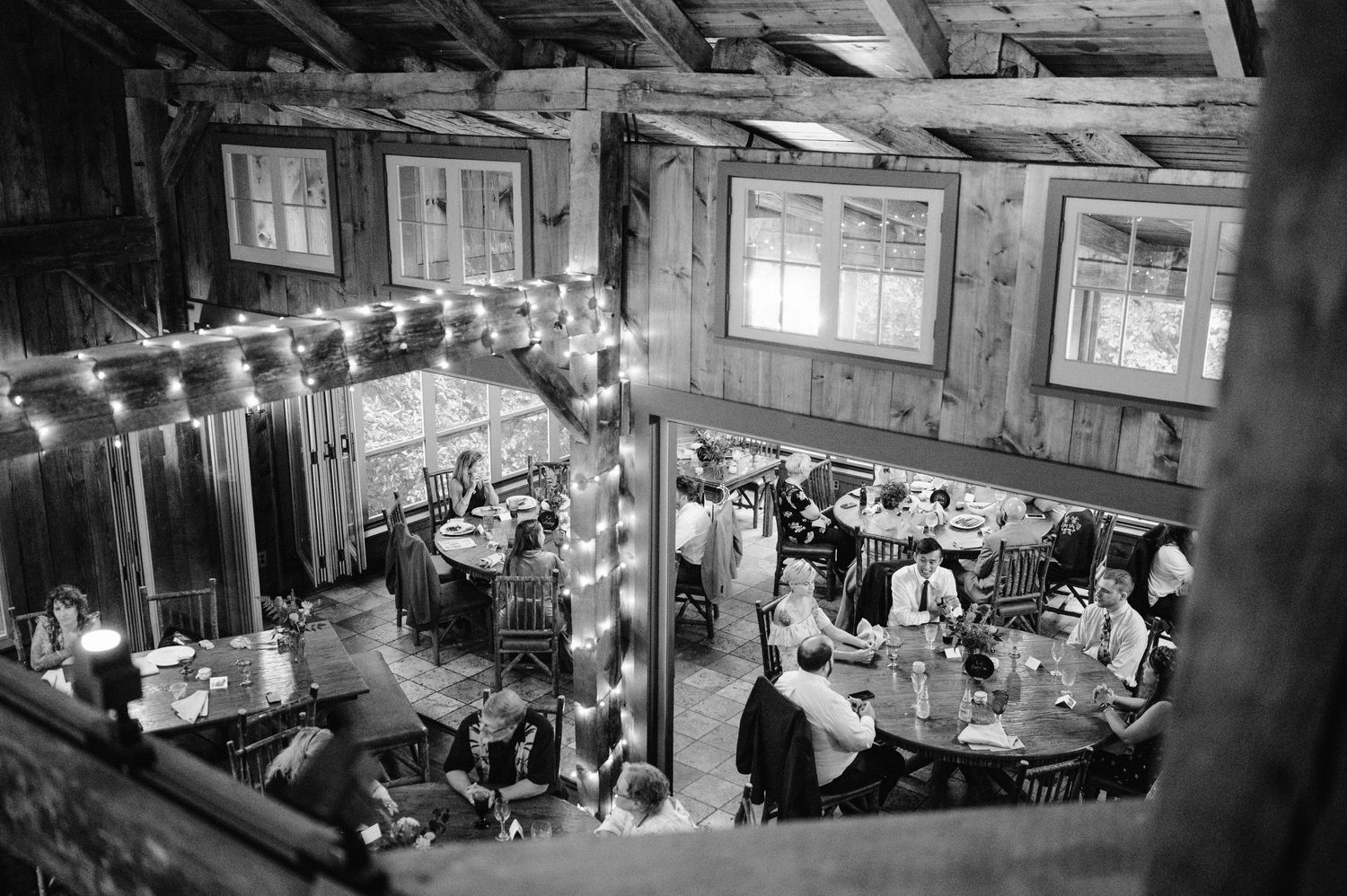 Black and white overhead view of a rustic reception venue with string lights and wooden beams.