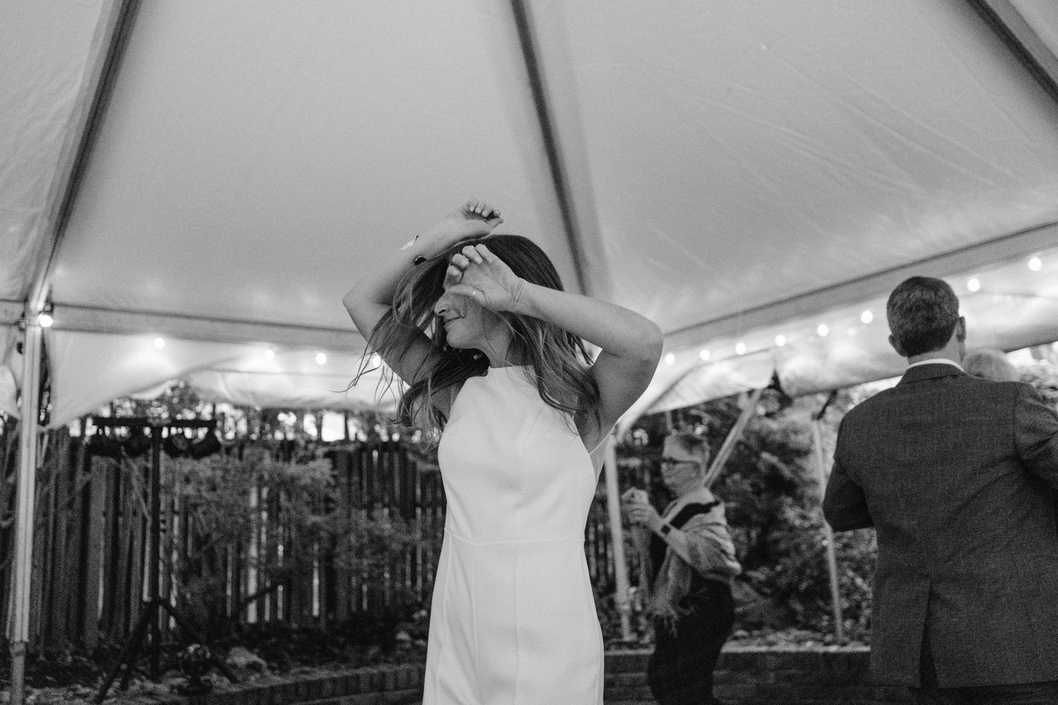 A person in a white dress dances energetically under a tent during a celebration.