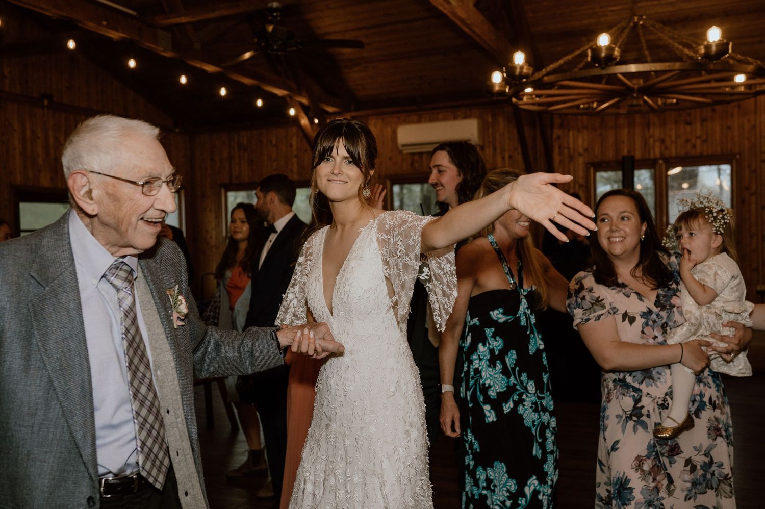 Wedding celebration with guests dancing in a rustic venue with string lights.