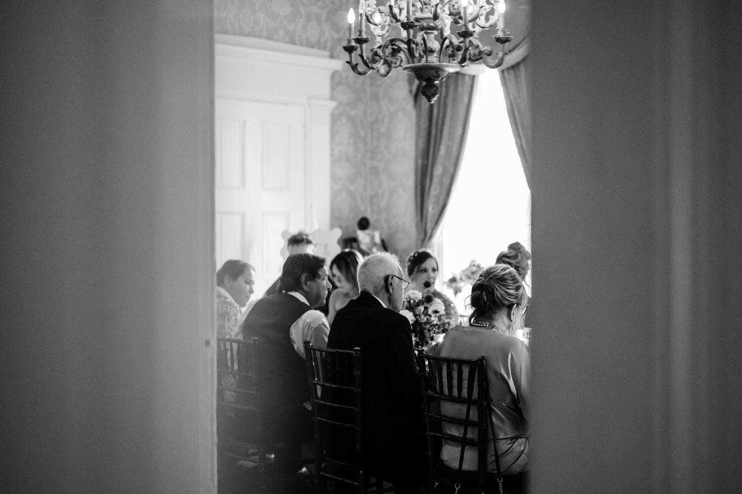 Candid black and white photo of wedding guests gathered in an elegant dining room.