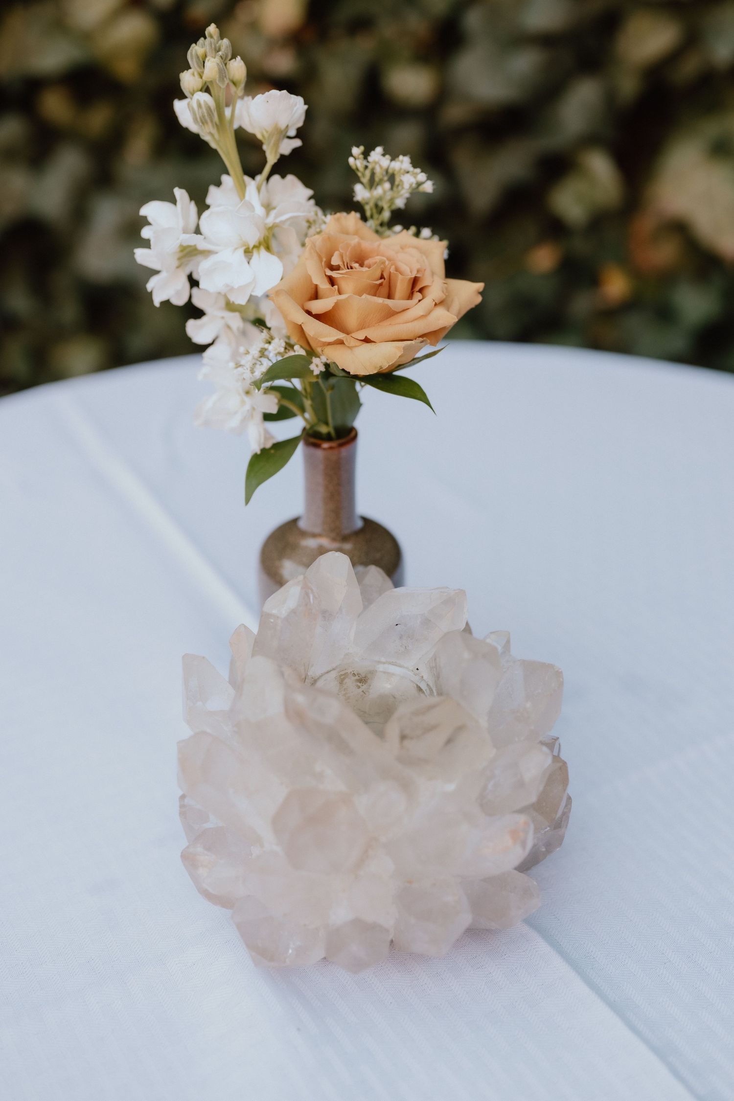 Small peach rose and white flower arrangement with crystal decoration on white tablecloth.