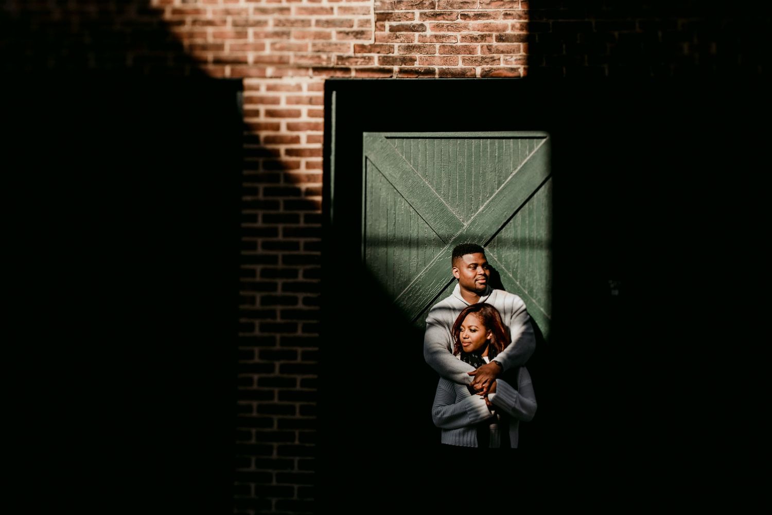 A couple embraces in a framed doorway of a brick building.