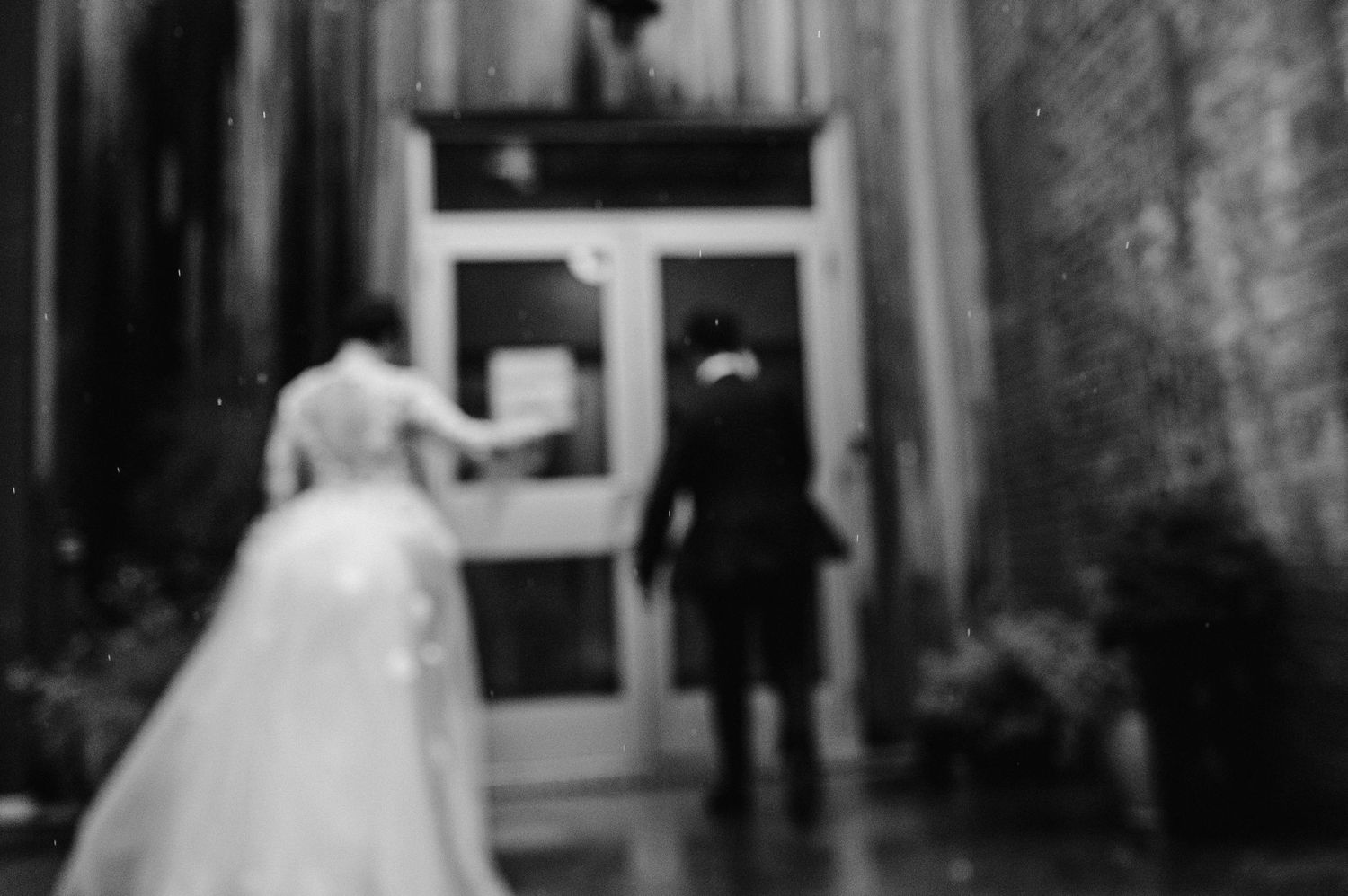 Blurred black and white image of couple entering doorway in formal attire.