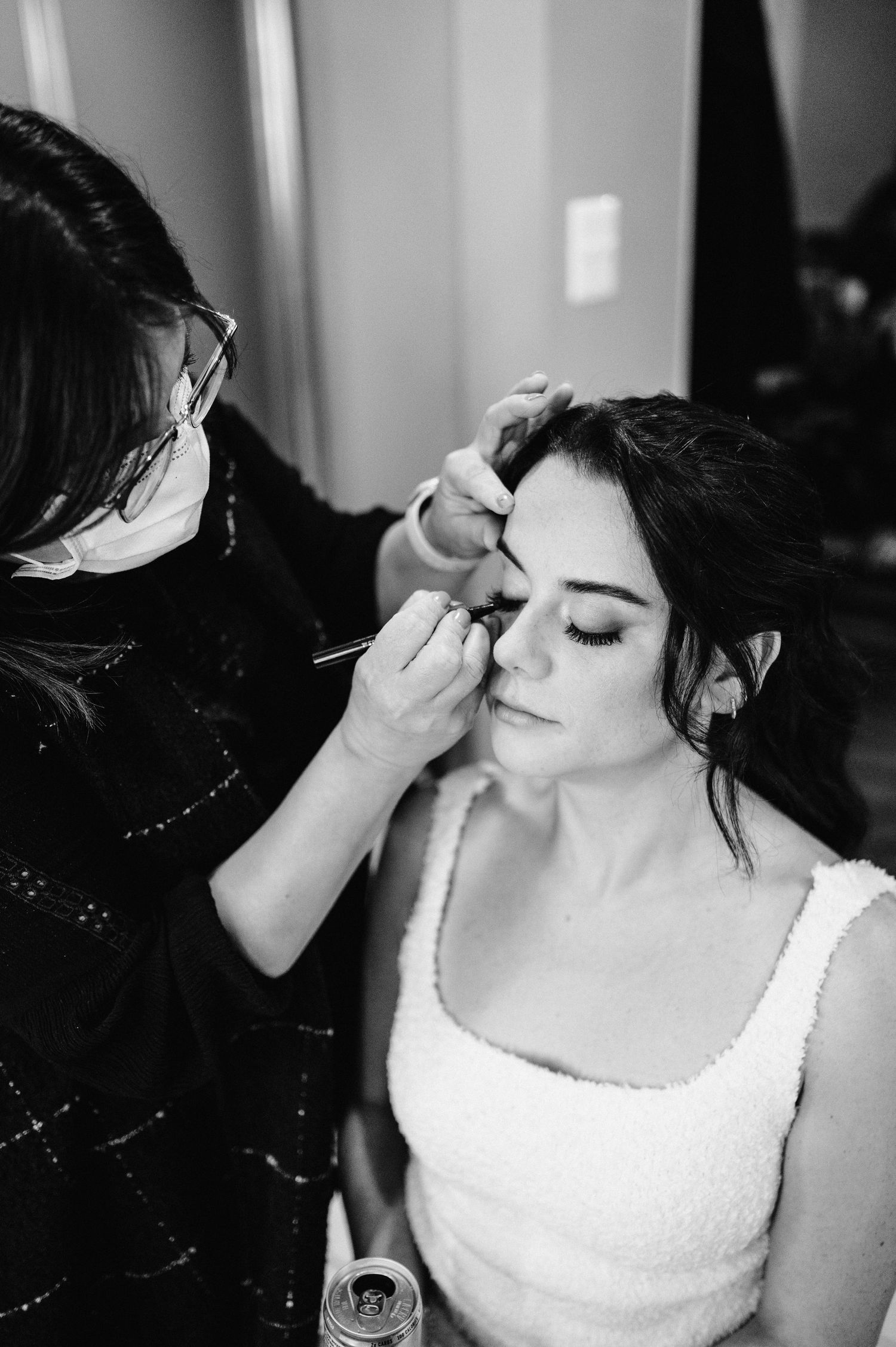 Black and white image of makeup application during wedding preparations.