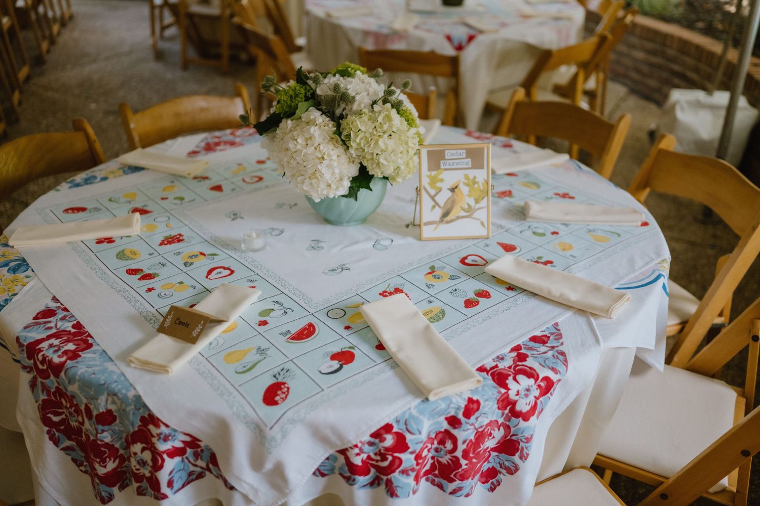 Wedding reception table with floral tablecloth and white centerpiece arrangement.