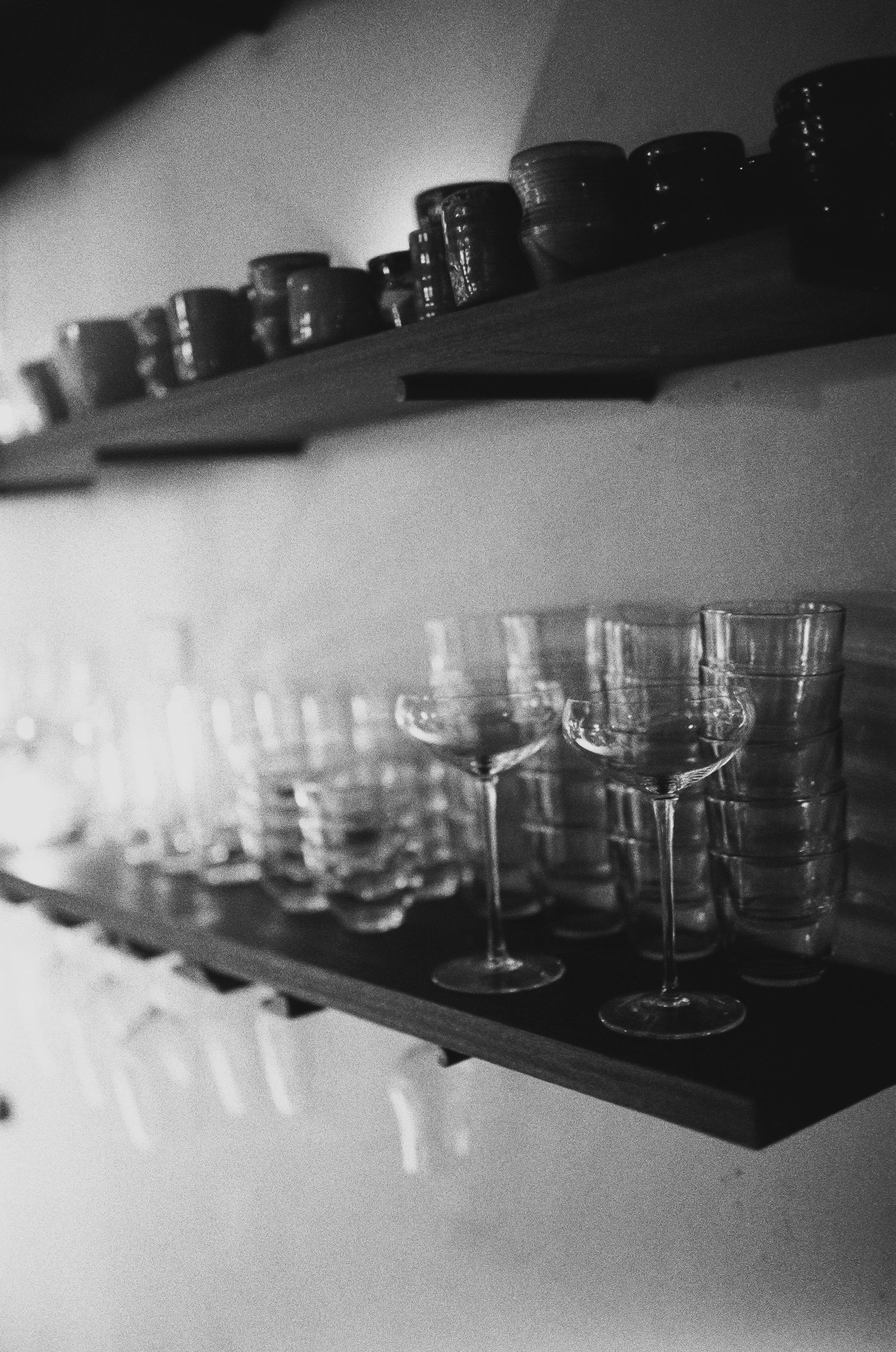 Row of vintage glassware displayed on dark shelves in black and white photography.