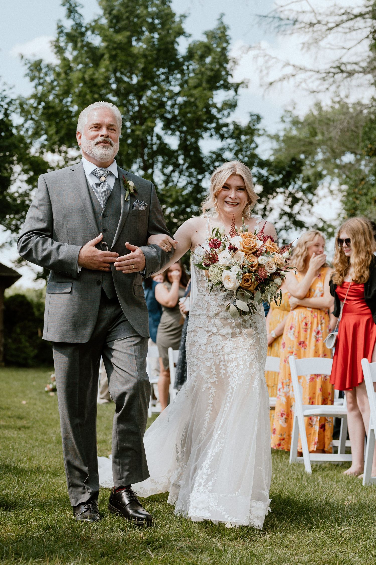 Wedding procession on green lawn with bride carrying colorful bouquet.