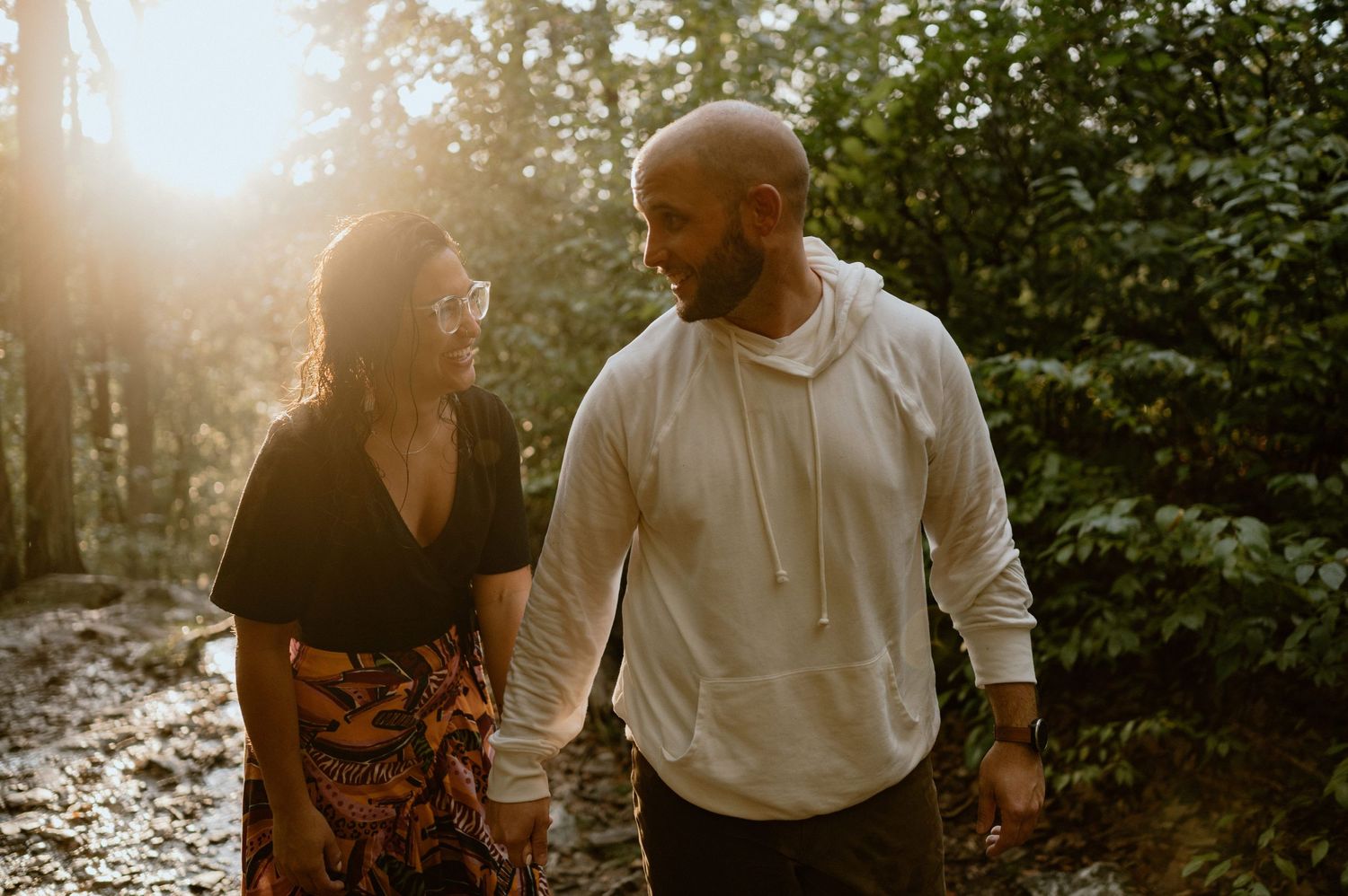 Couple walking together on sunlit forest path during golden hour.