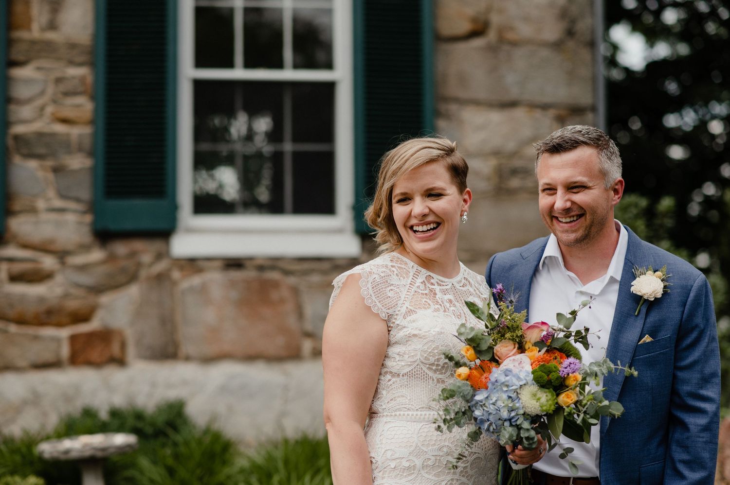 A sunny outdoor wedding moment with a bright summer bouquet featuring orange and blue flowers.