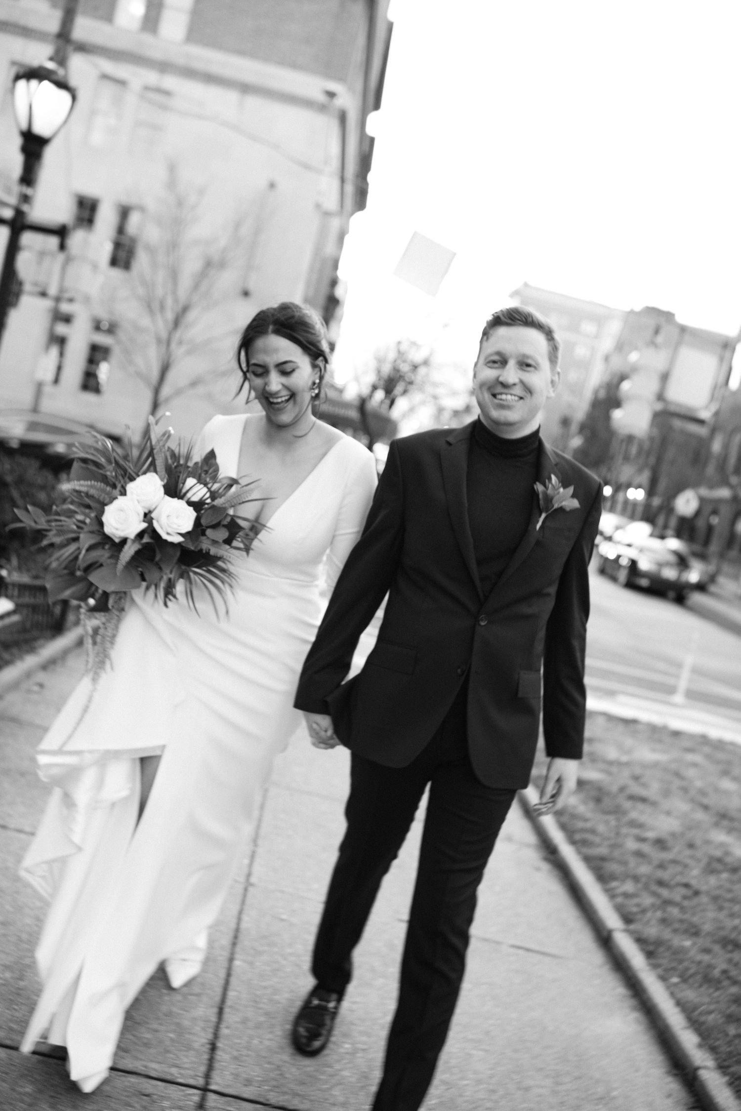 Candid wedding photo on urban street with couple walking and laughing together.