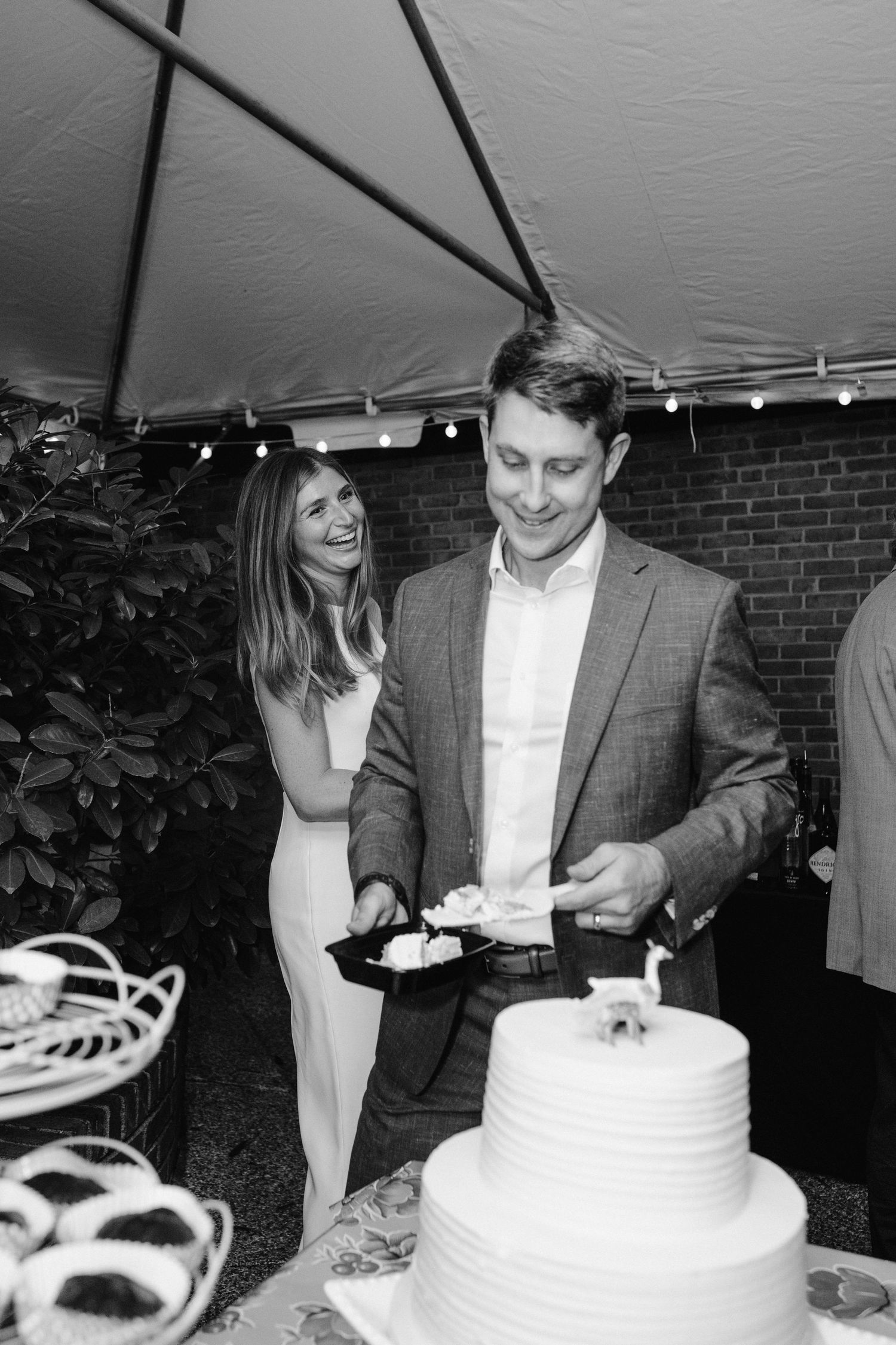 Black and white photo of couple serving their tiered wedding cake at reception.