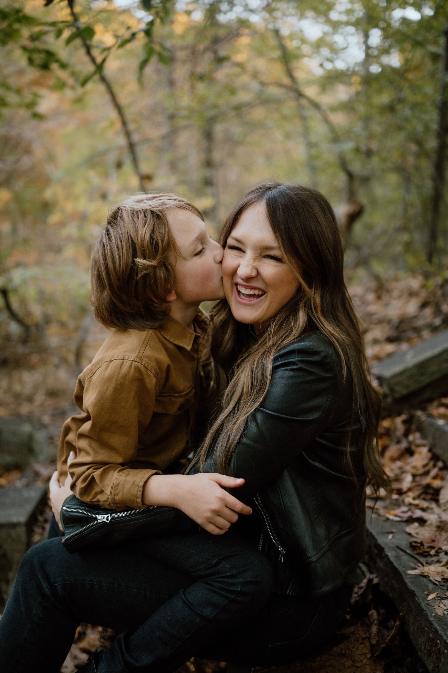 A candid moment of joy and affection captured in a wooded autumn setting.
