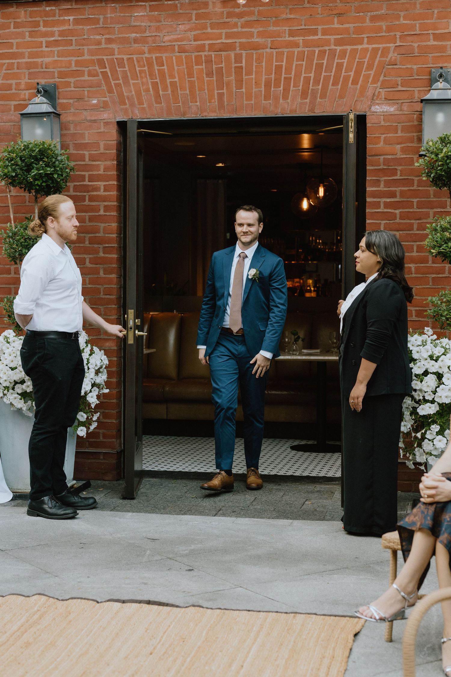 People gathered at a brick entrance doorway decorated with white floral arrangements.
