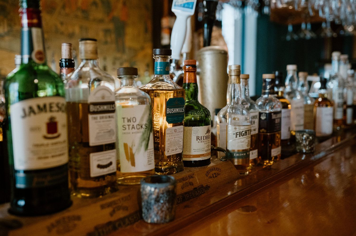 Collection of whiskey bottles lined up on wooden bar counter.