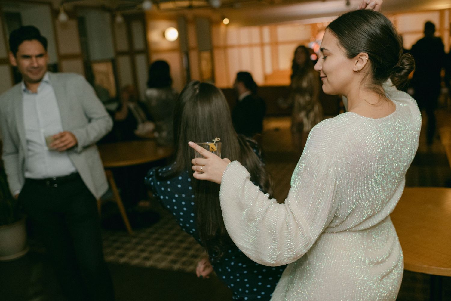 A woman in a white sweater enjoying drinks at an indoor gathering.