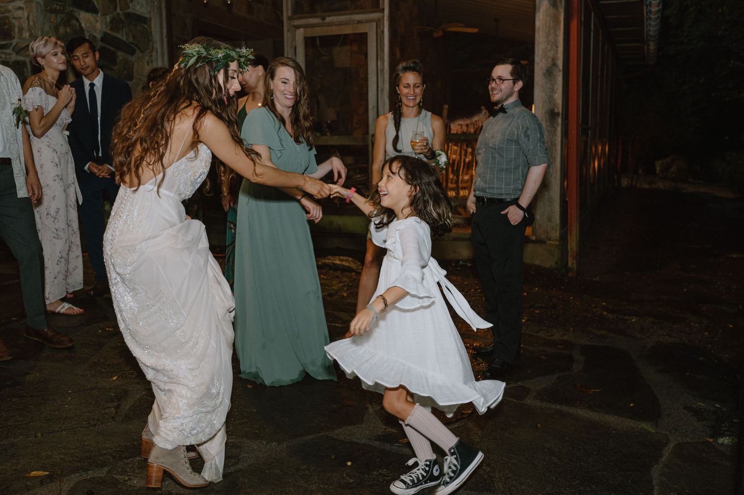 Wedding guests dancing with a young flower girl in a white dress on a stone floor.