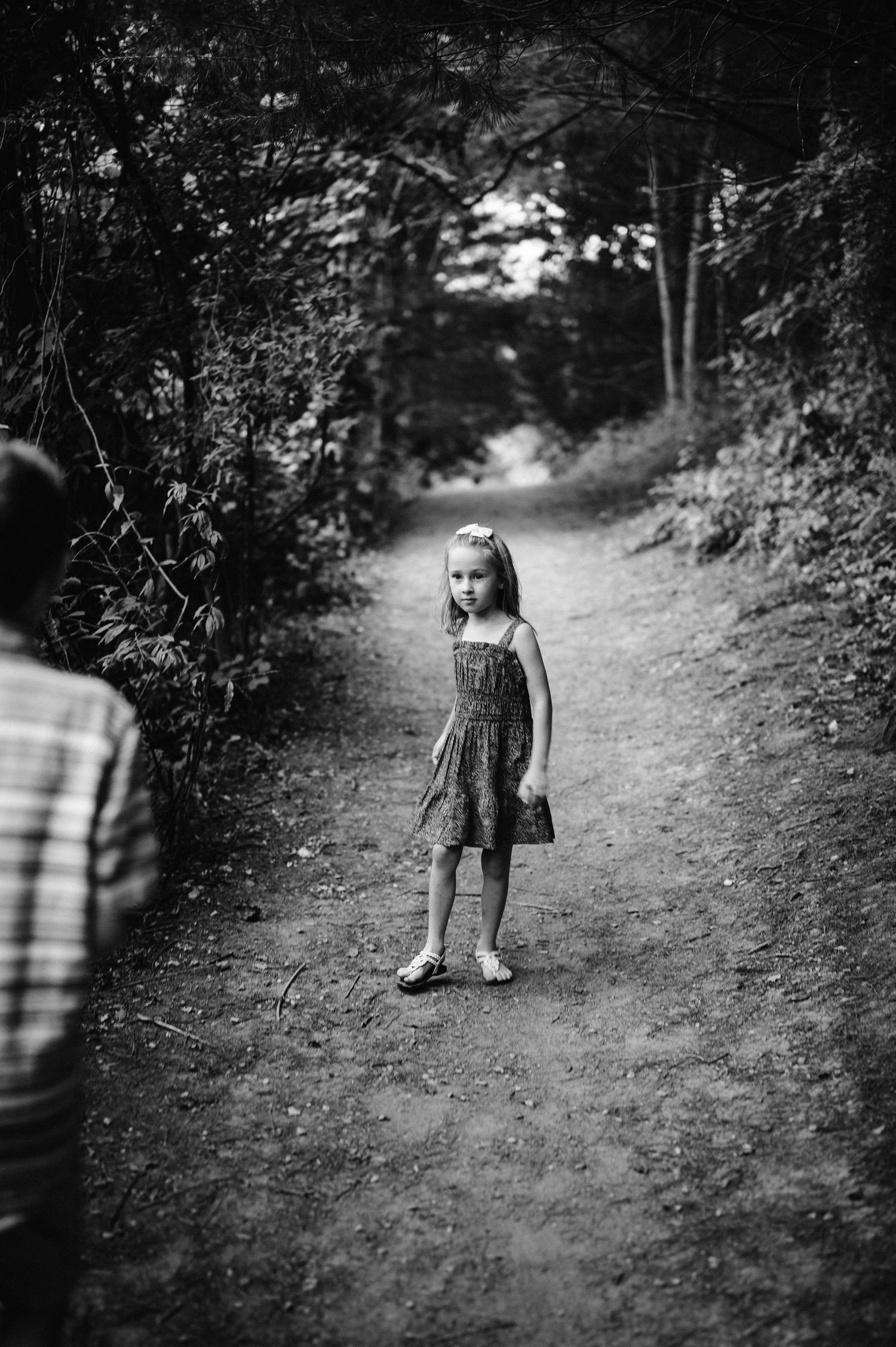 A child stands alone on a wooded dirt path in black and white.
