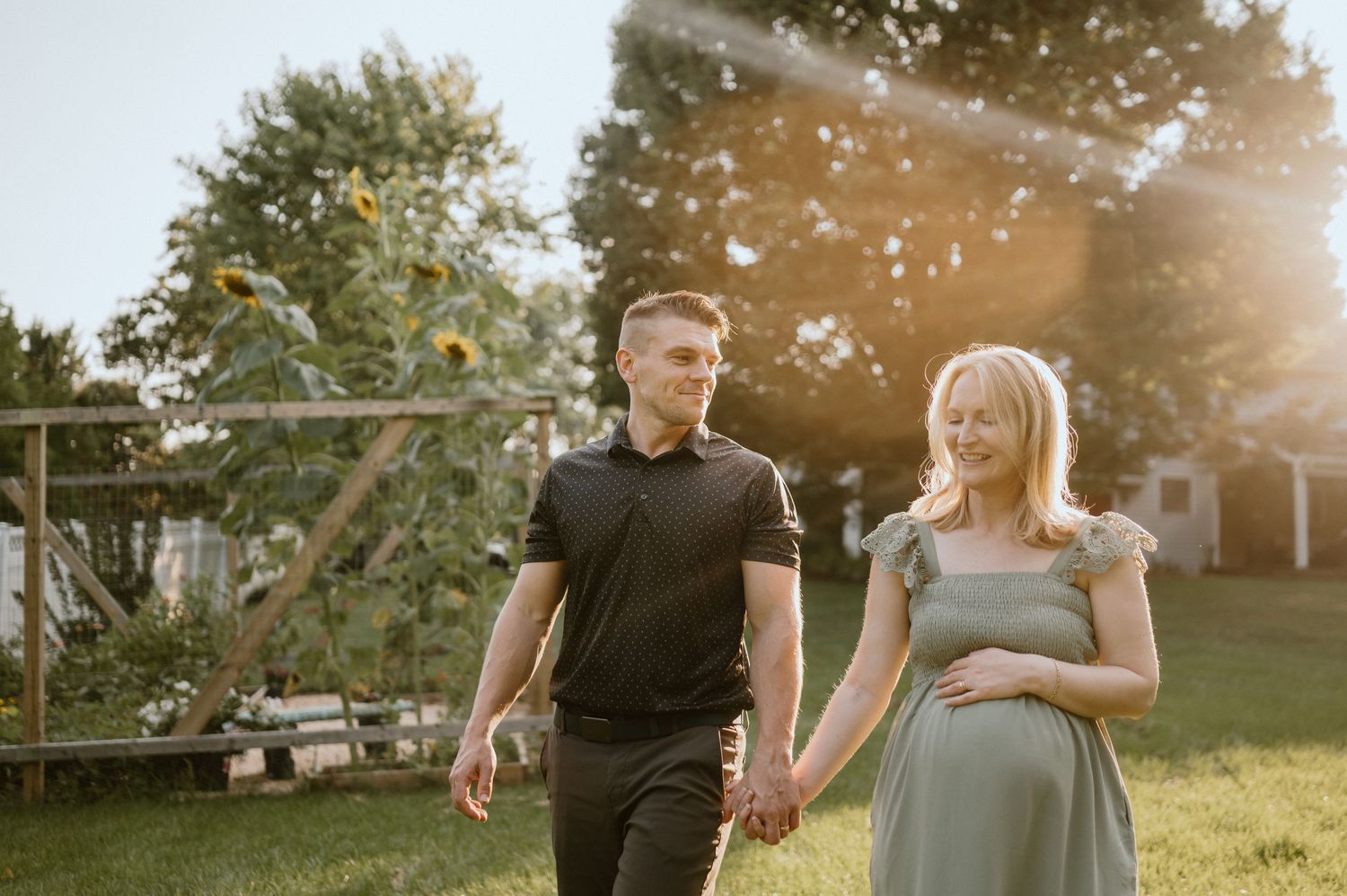 A couple walking hand in hand through their garden during golden hour.