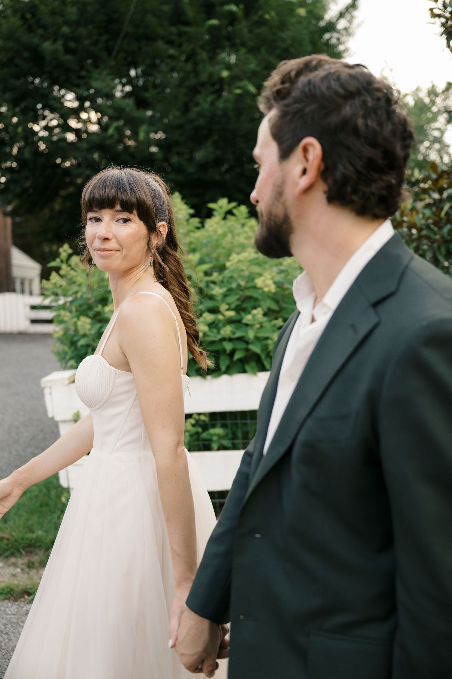 A couple at an outdoor wedding poses together in natural lighting against a green garden backdrop.