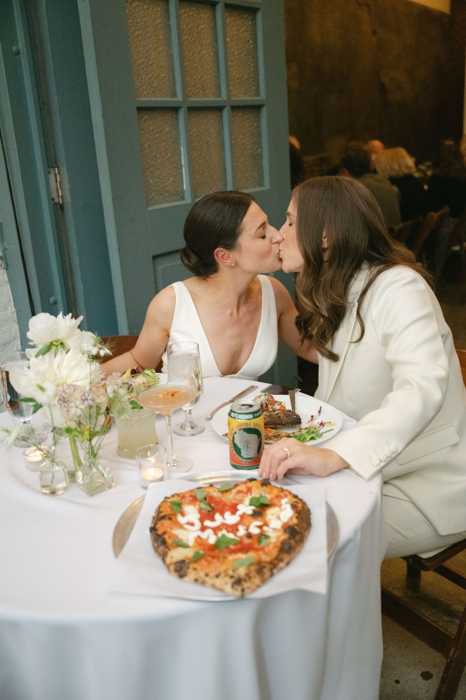 Two people share an intimate dining moment at an outdoor restaurant table with pizza and floral centerpiece.