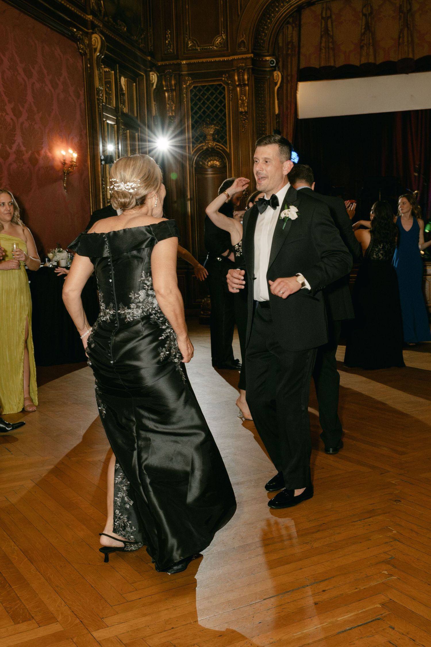 Couples dancing at a formal event in a luxurious wood-paneled ballroom with warm lighting.