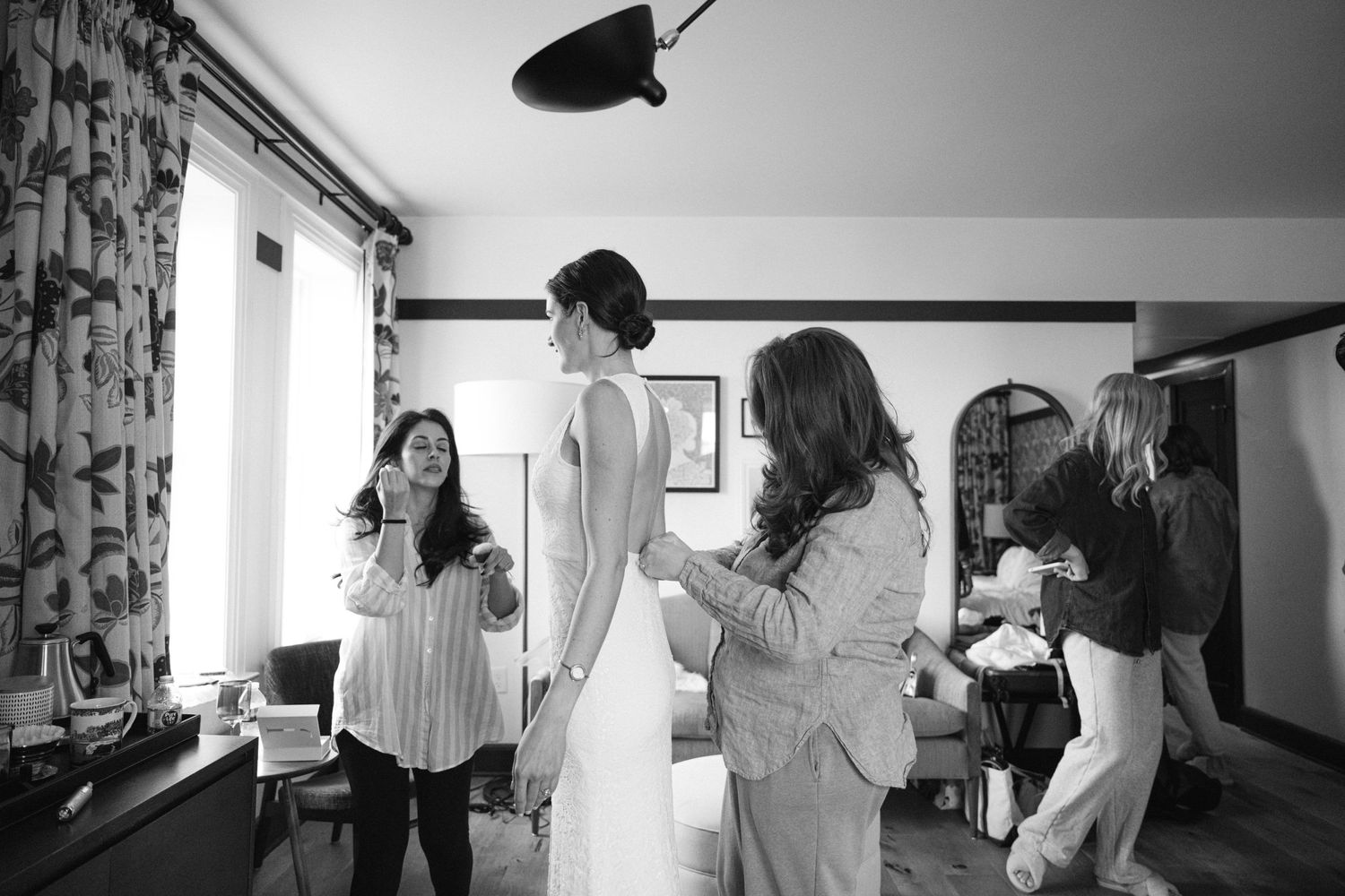 A candid black and white preparation scene in a room with floral curtains and natural lighting.