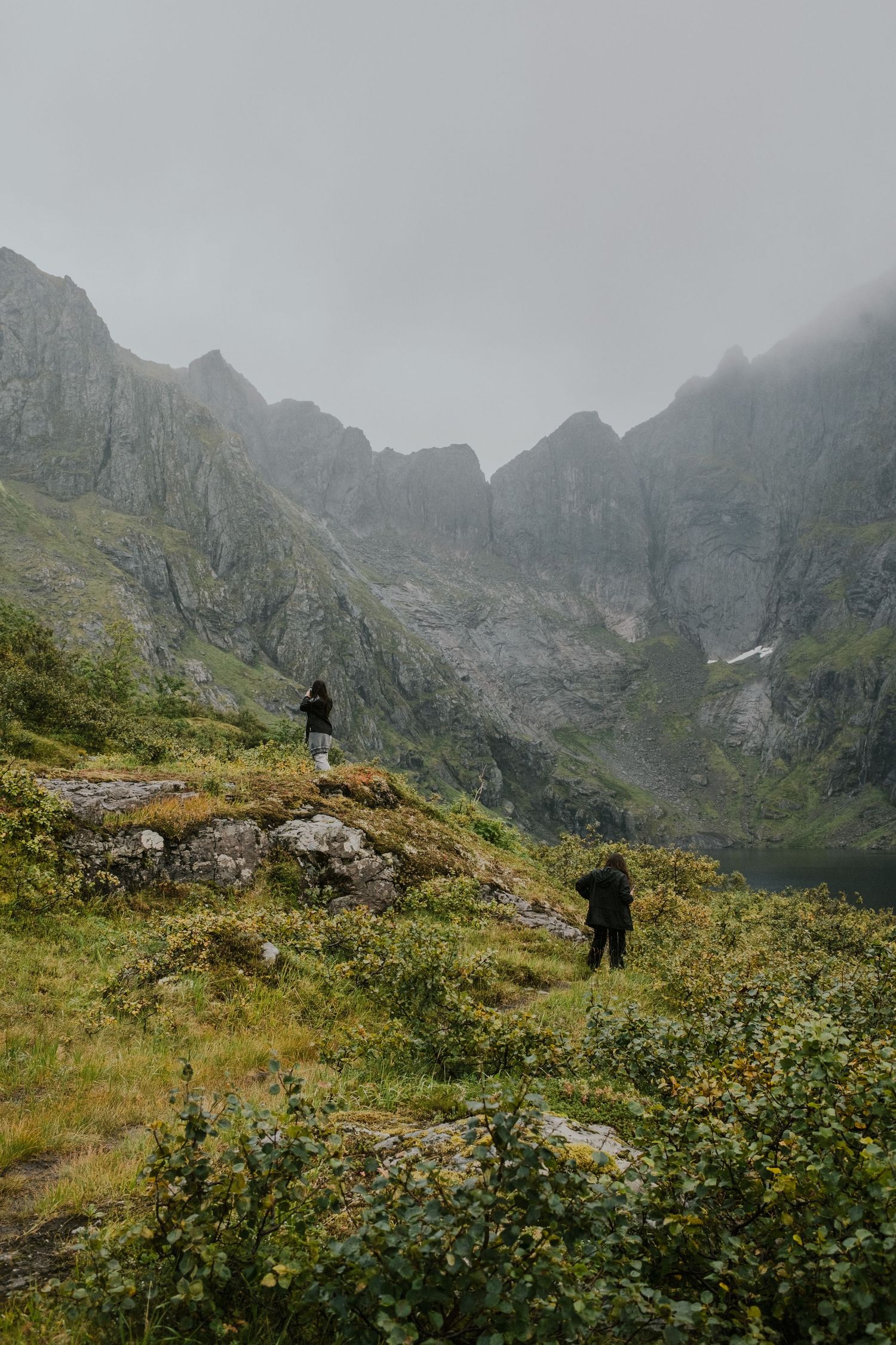 Adventurers hiking through alpine terrain with steep mountain valleys and cloudy skies.