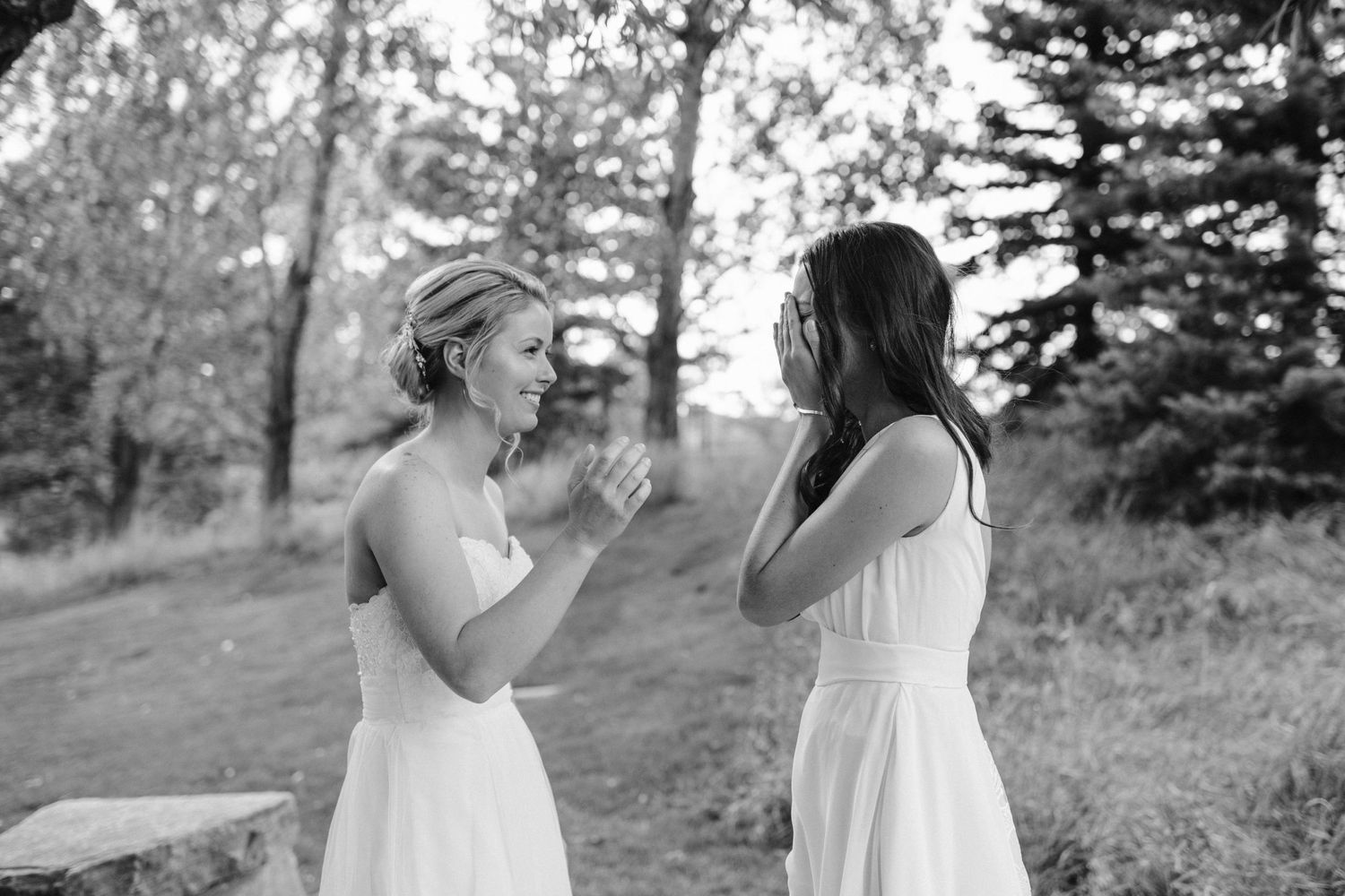 Two people in white dresses share an emotional moment outdoors.