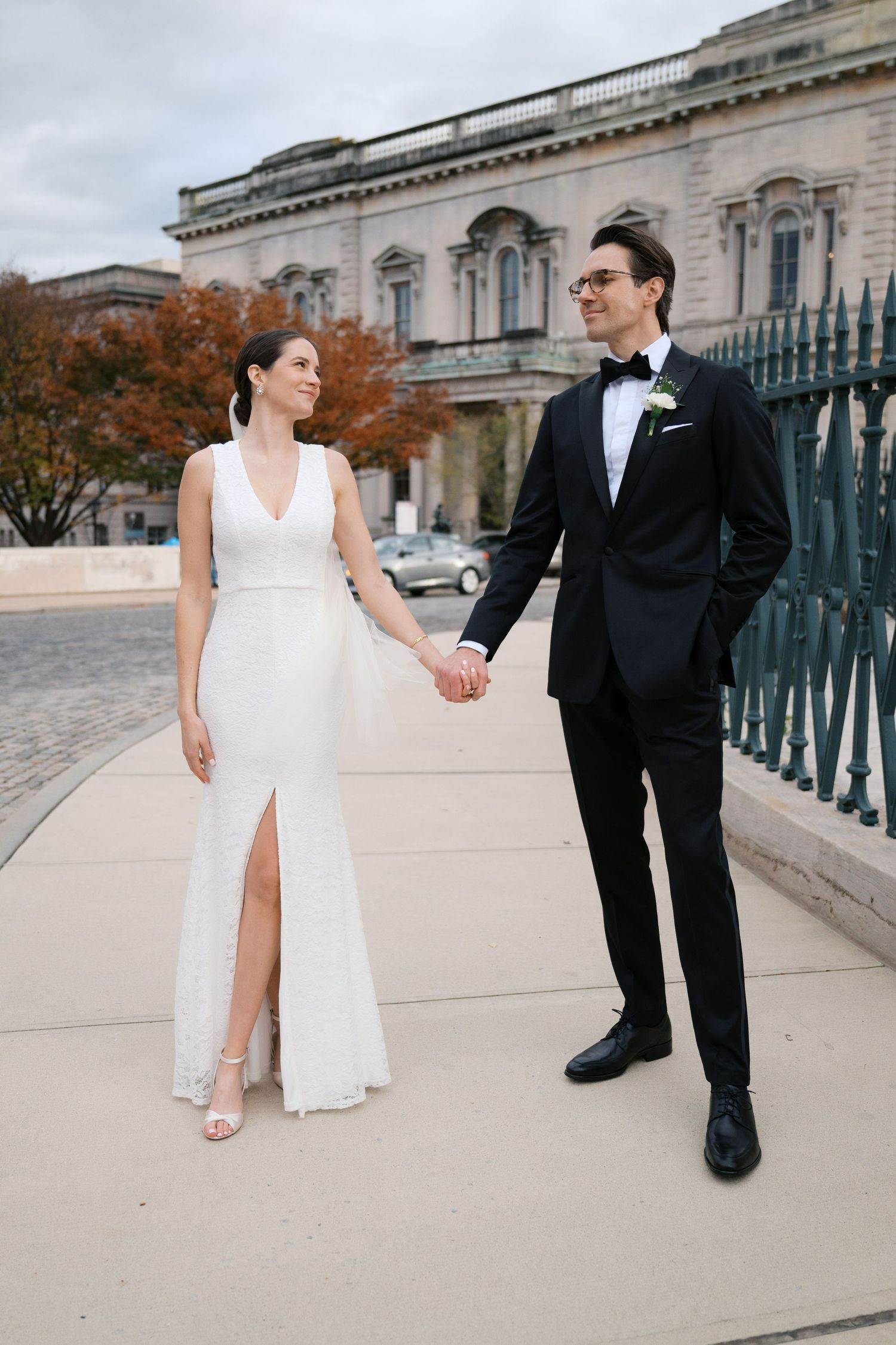 Elegant couple in wedding attire pose together on historic building grounds during autumn.