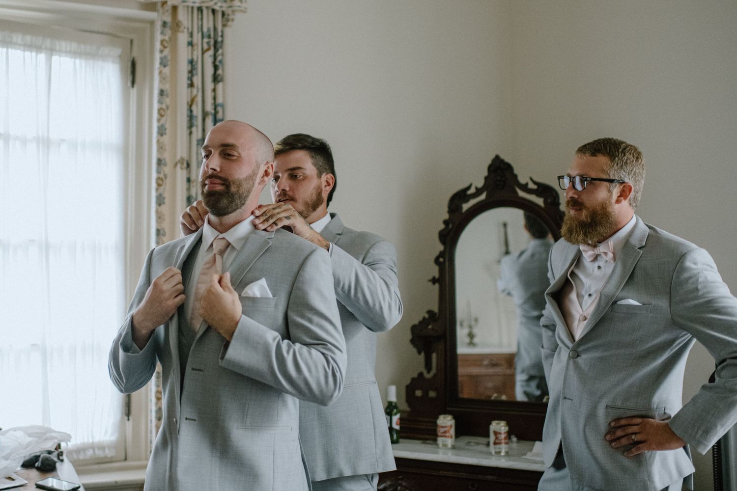 groomsmen helping groom get dressed