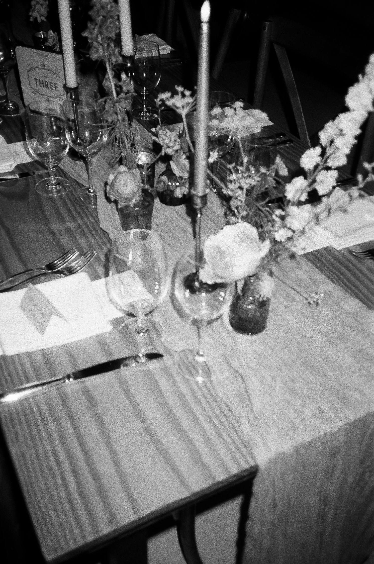 Elegant wedding reception table setup with candles, wine glasses and floral arrangements in black and white.