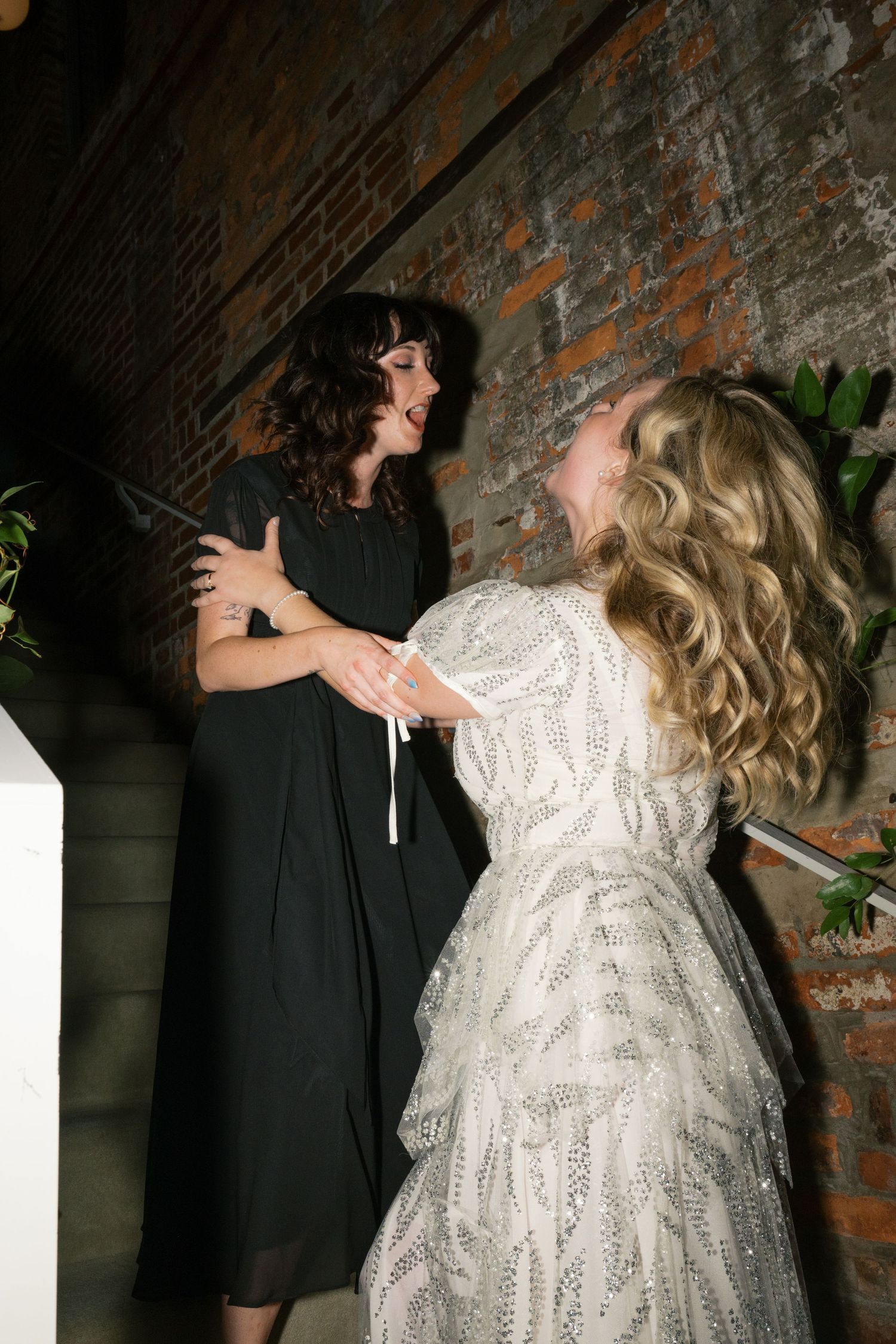 Two people dancing and interacting near exposed brick wall in contrasting black and white outfits.