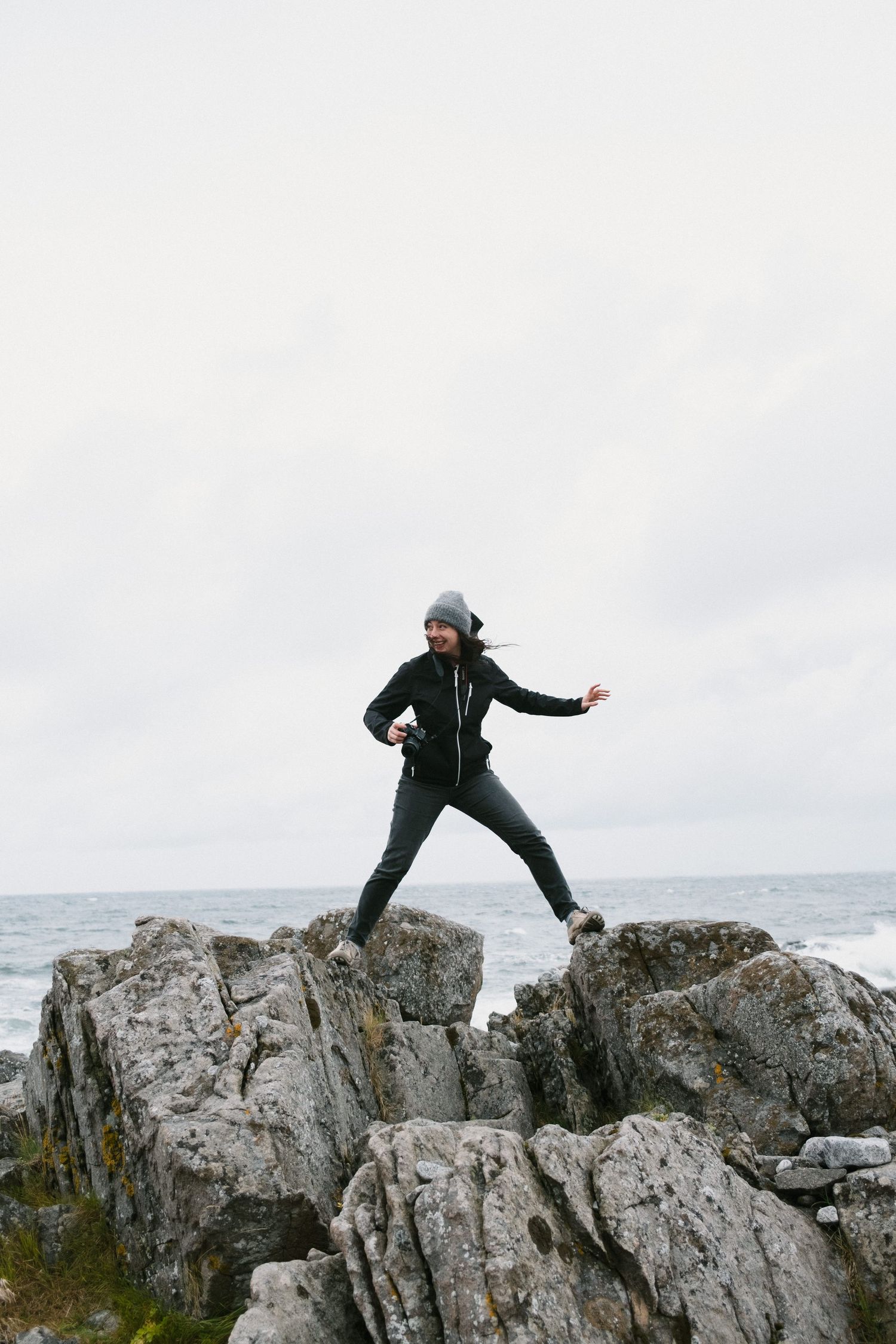 Figure in dark clothing jumps between rocky coastal formations by the ocean.