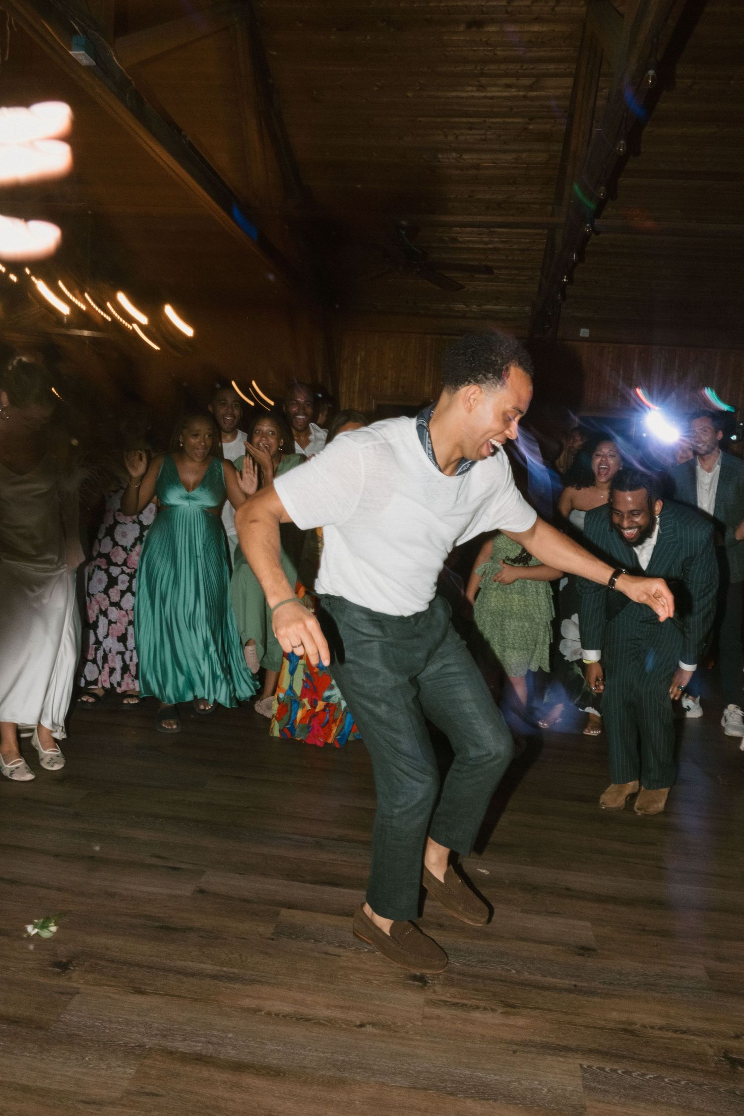 A wedding guest shows off enthusiastic dance moves on a wooden floor.
