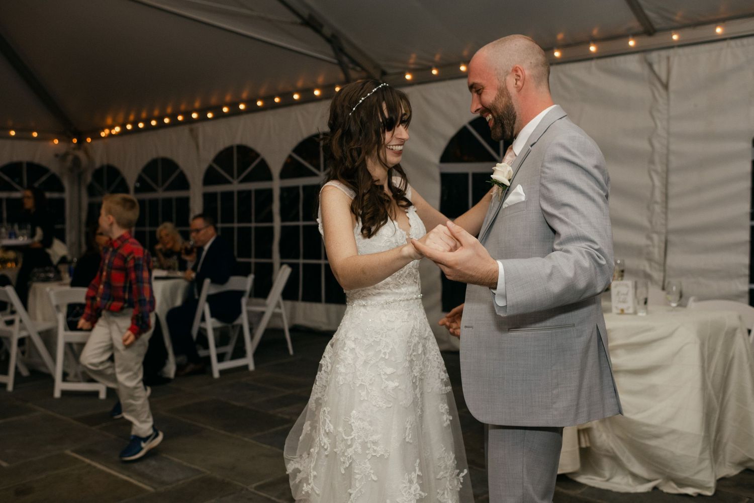 A couple shares an intimate dance moment under a tented wedding reception with string lights.
