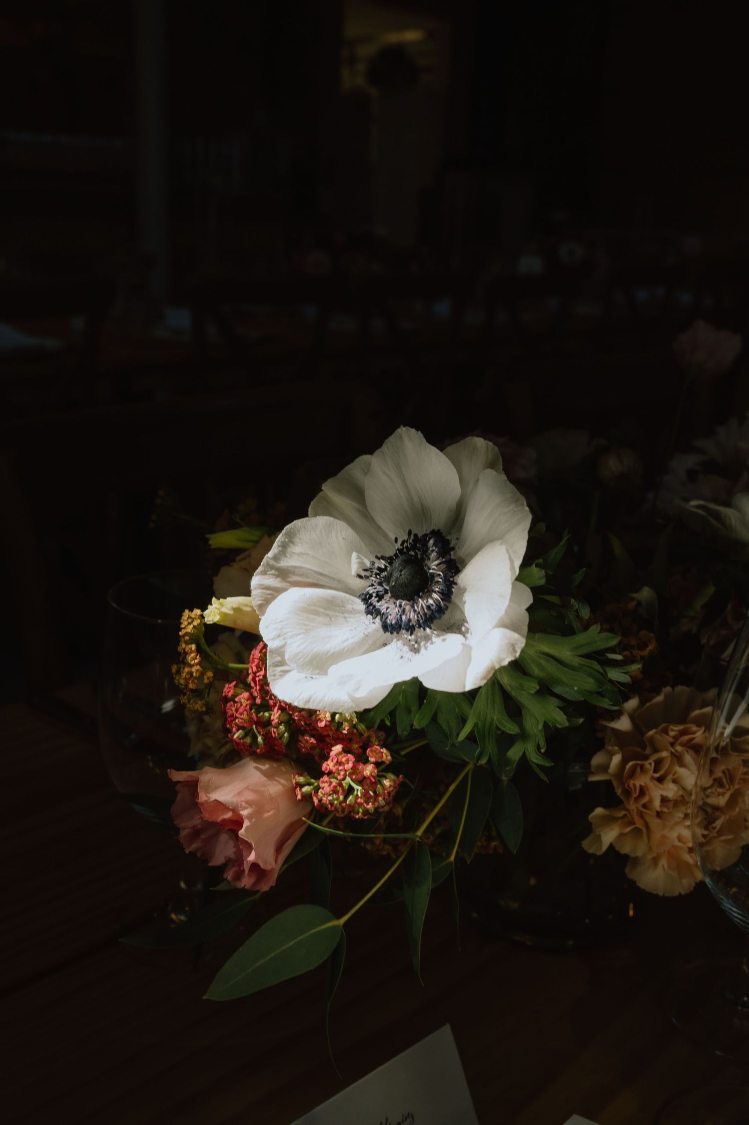 Close-up of white anemone flowers with dark centers arranged with other blooms in dramatic lighting.