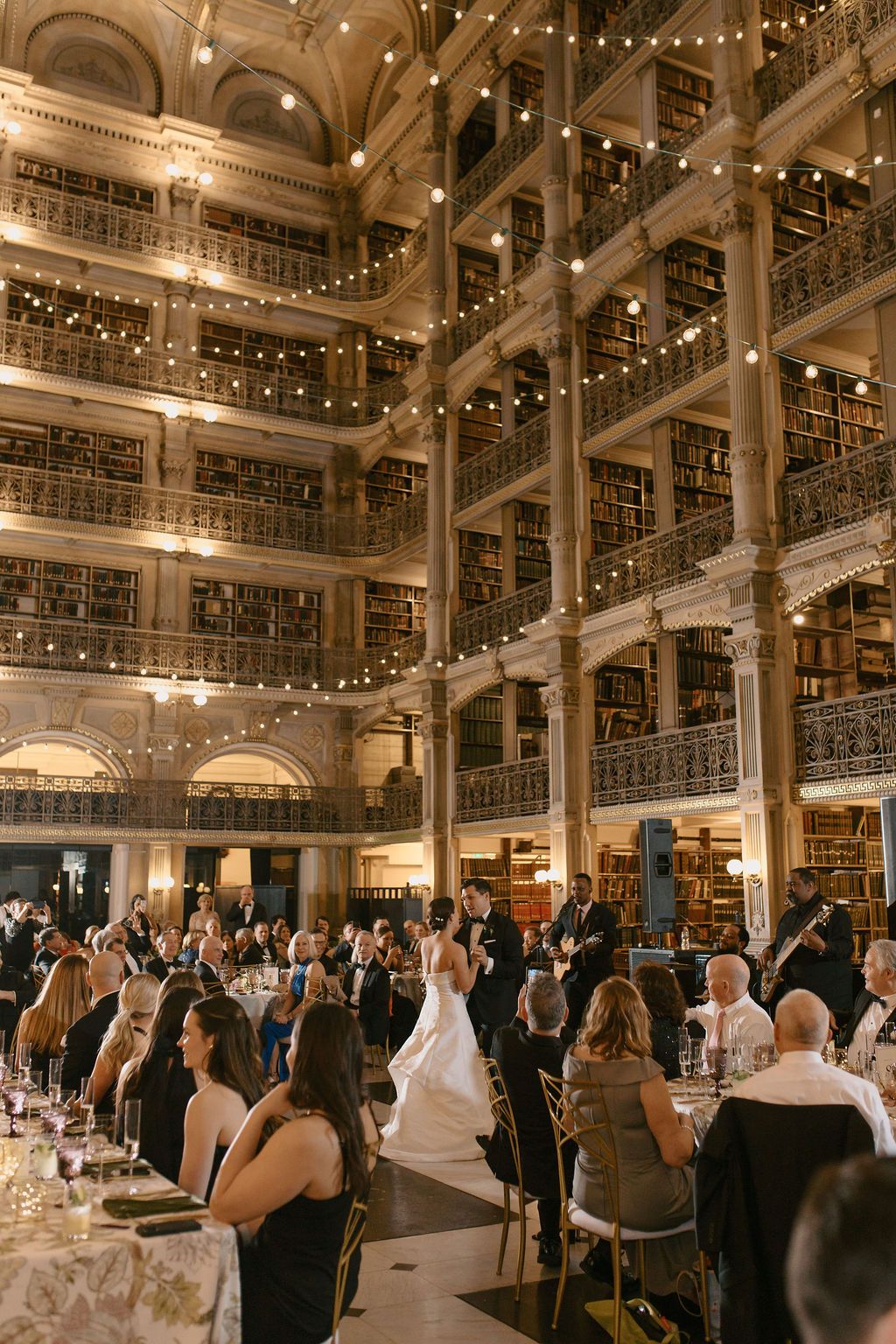 Wedding reception in a multi-level historic library with string lights and elegant table settings at George Peabody Library Wedding in Balti