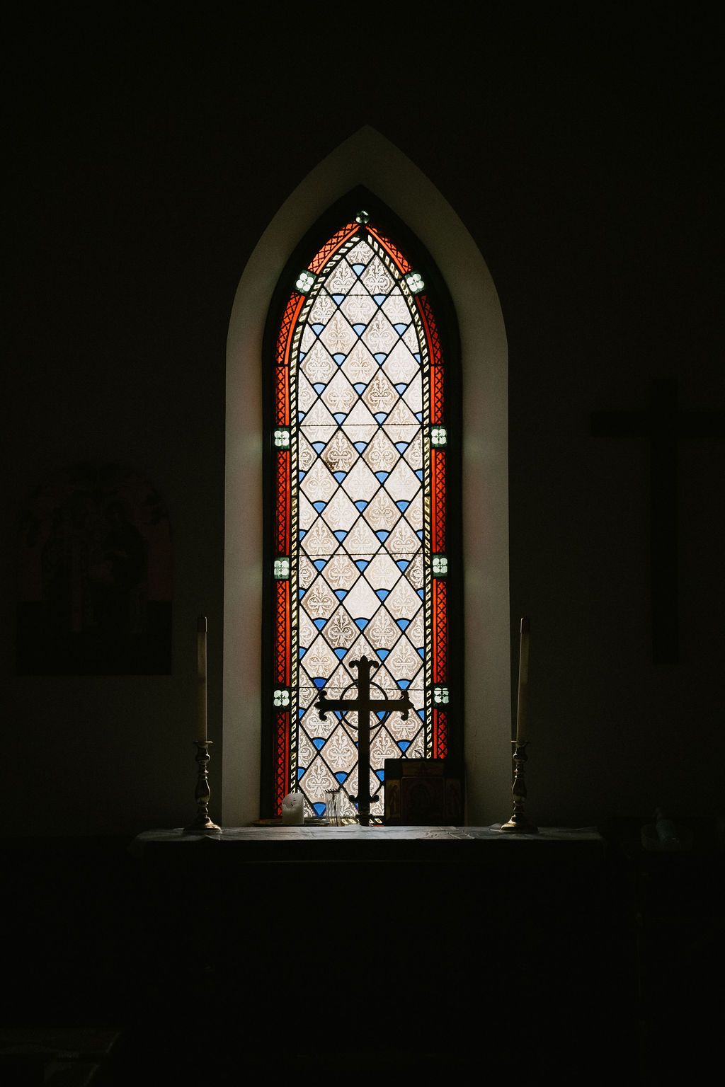 Gothic stained glass church windows with ornate patterns casting dramatic light in a dark interior.