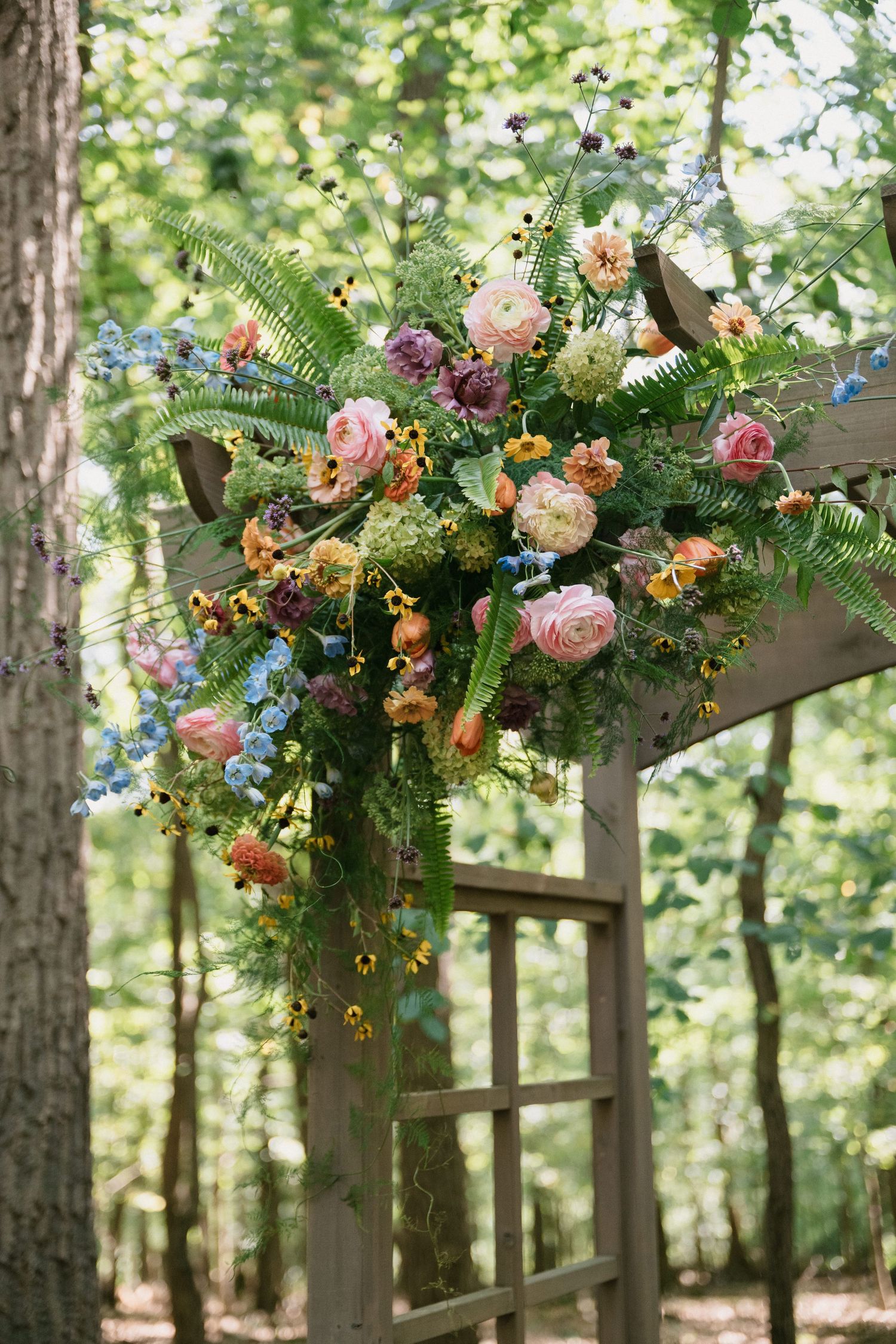 Colorful floral arrangements with roses and mixed flowers decorating a wooden wedding arch.