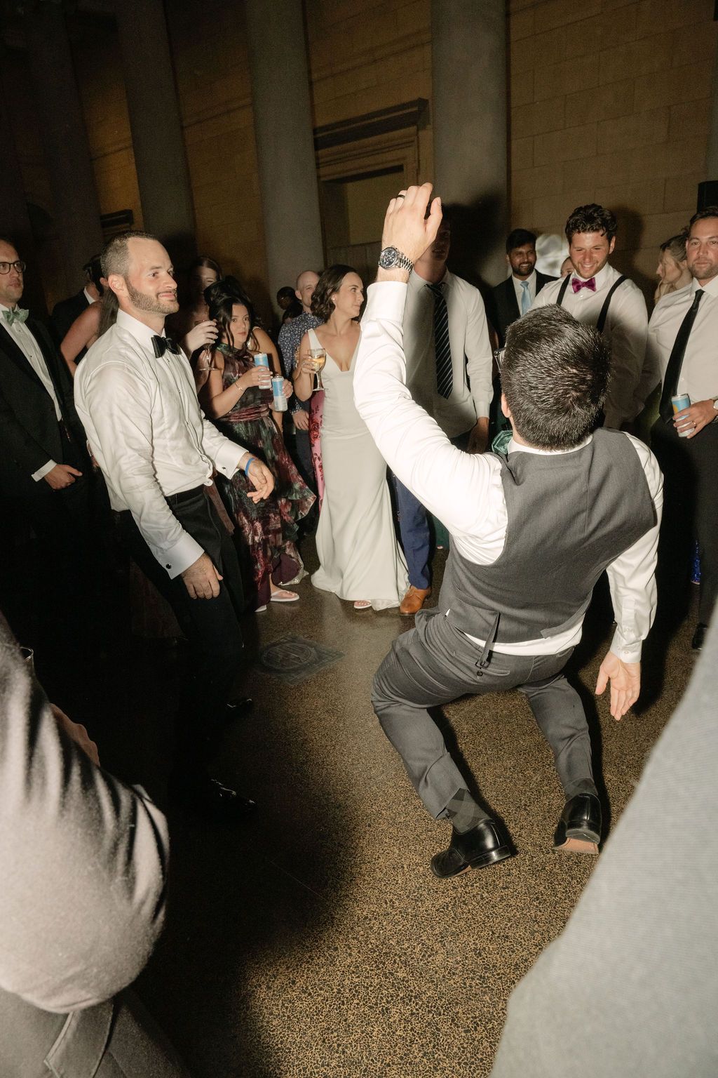 People dancing and celebrating at a wedding reception on a speckled floor under dim lighting.