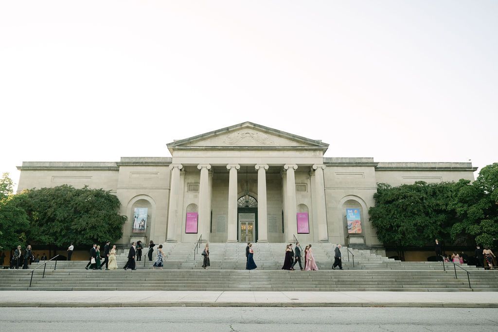 The Baltimore Museum of Art features a grand neoclassical facade with tall columns and visitors on its front steps.