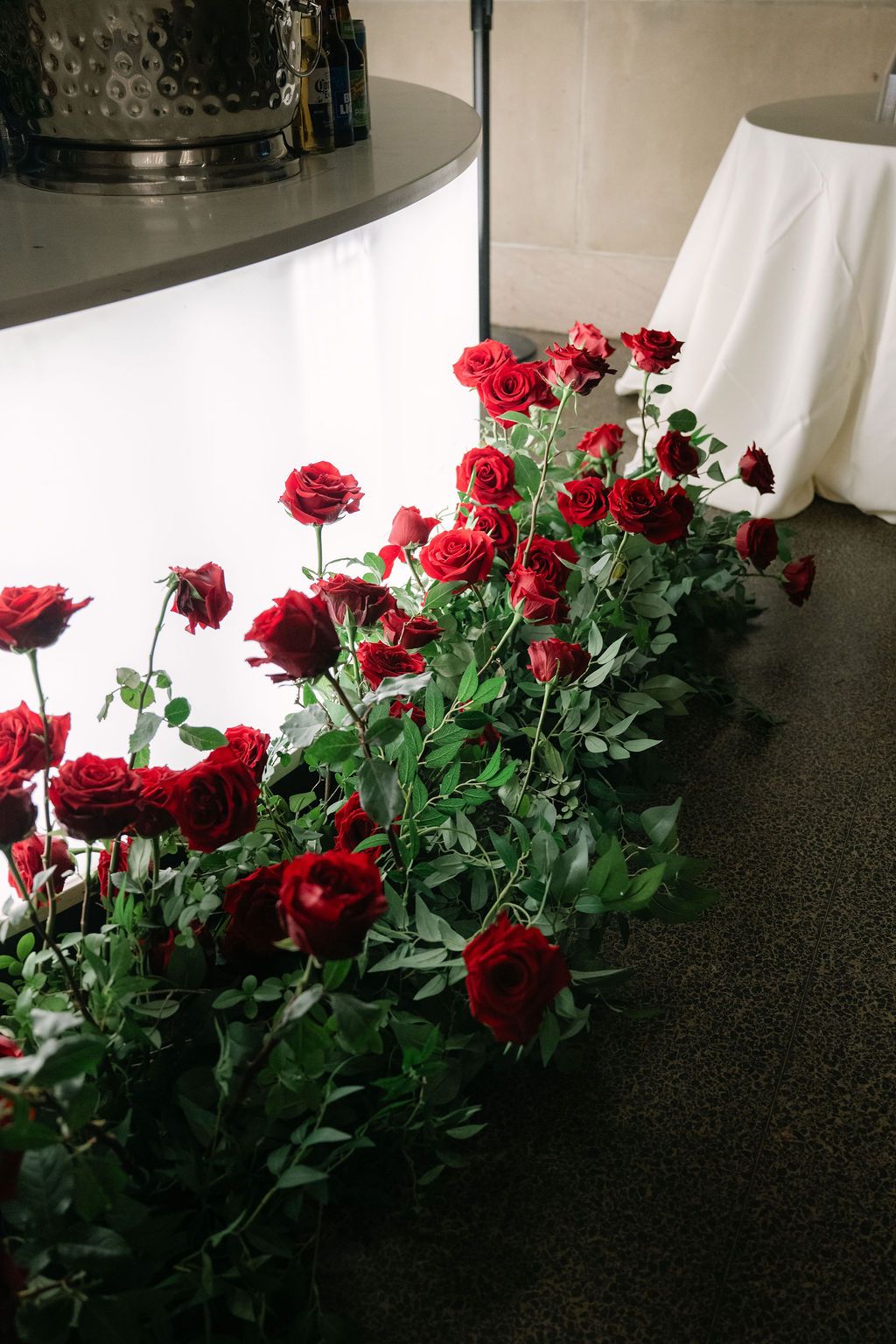 A collection of deep red roses with green foliage arranged against a dark countertop in natural window light.