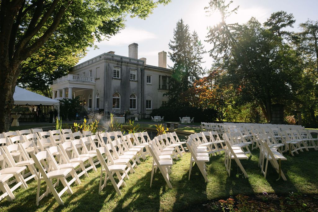 White chairs arranged in rows for an outdoor wedding ceremony with sunlight filtering through trees.