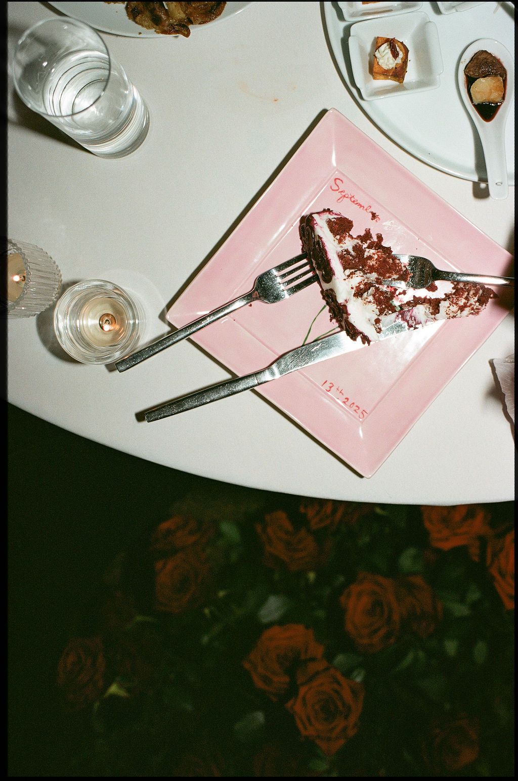 Pink napkins and wine glasses are arranged on a dark floral tablecloth in a restaurant setting.