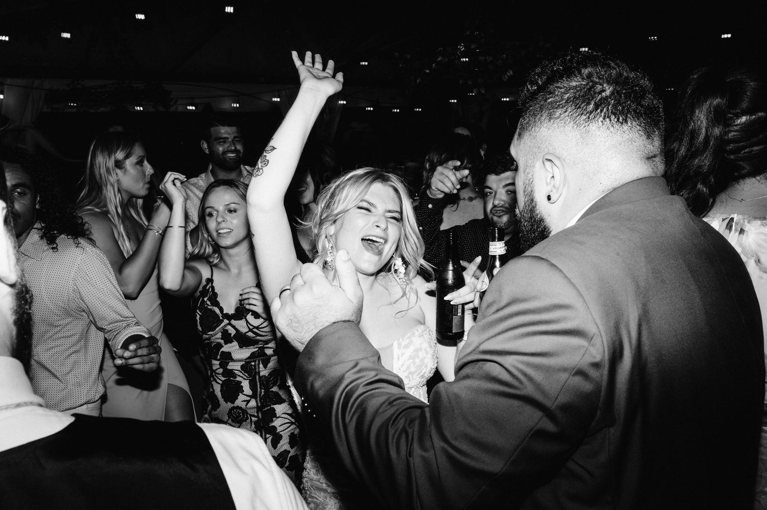 Black and white photo of wedding guests dancing enthusiastically at a reception celebration.