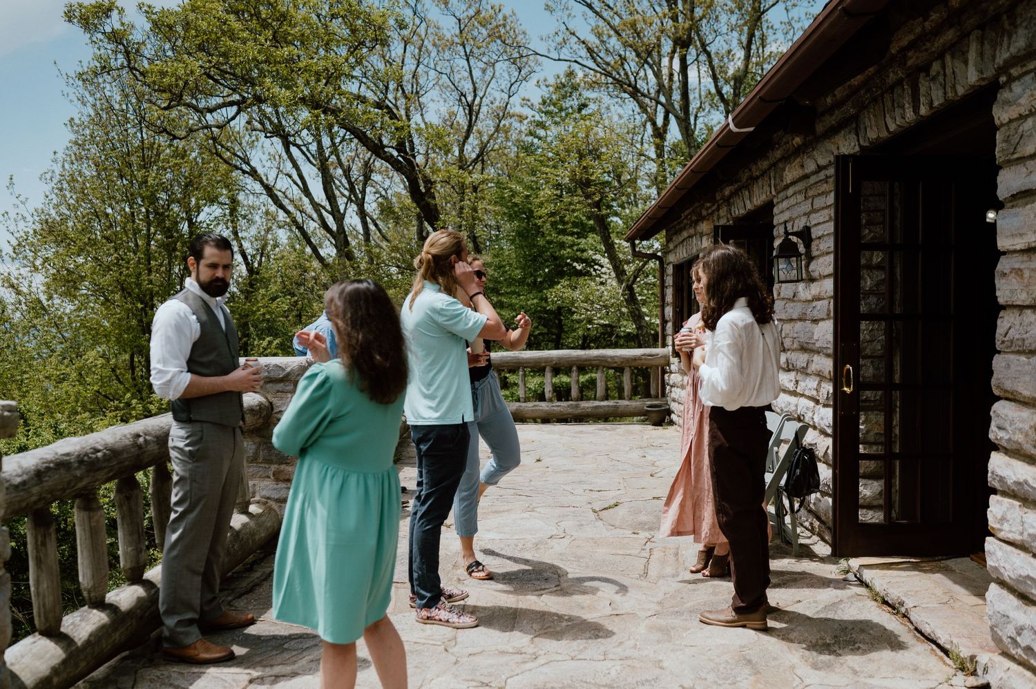 Small group gathered on stone patio outside rustic mountain lodge on sunny day.