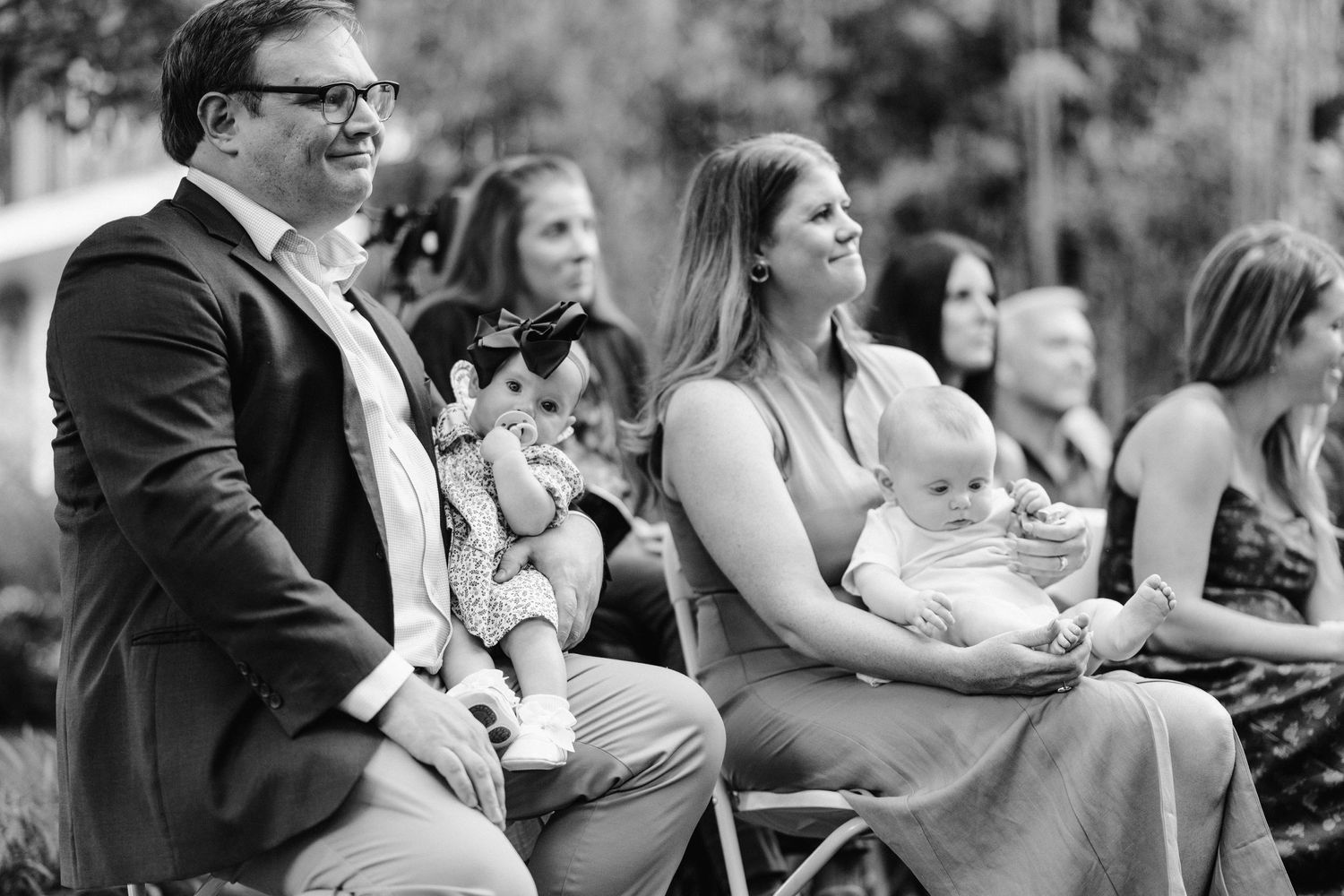 Black and white photo of guests holding babies while seated at an outdoor event.