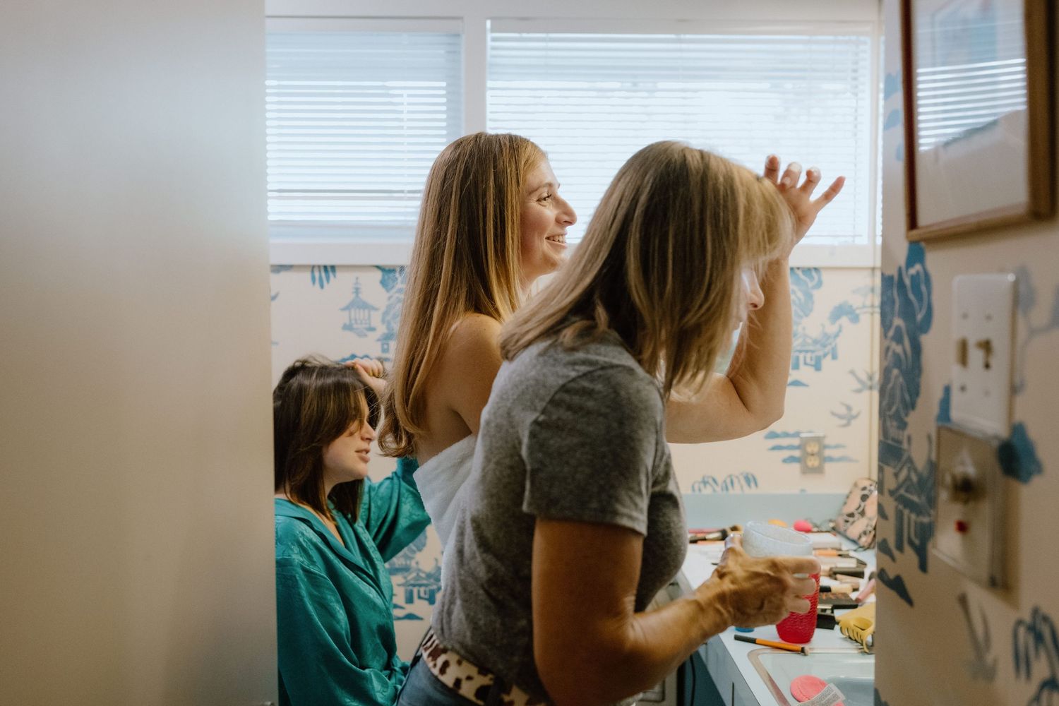 People preparing in bathroom with floral wallpaper and natural window light.
