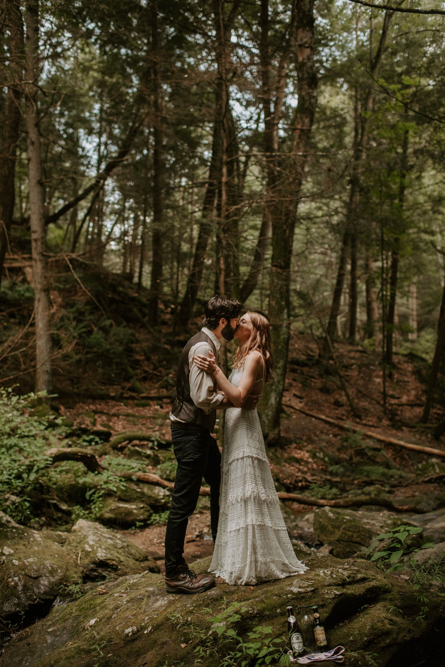 A romantic woodland wedding scene with a couple standing on mossy rocks in a forest.