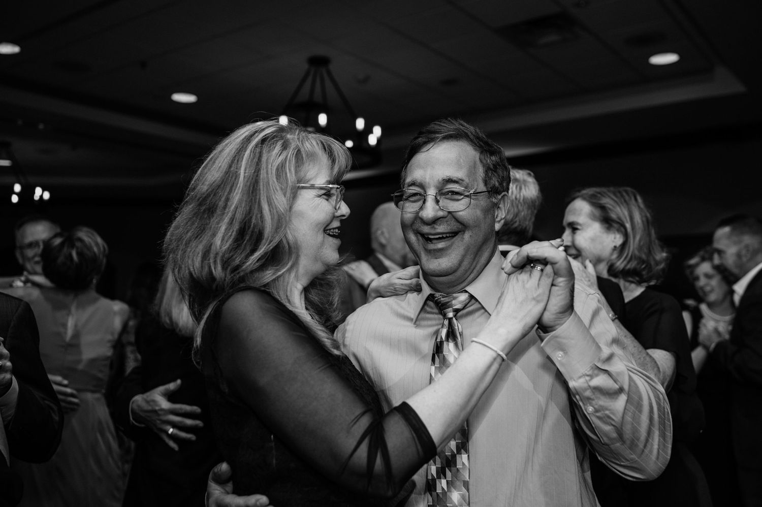 Guests sharing a joyful dance moment at indoor reception with chandeliers.